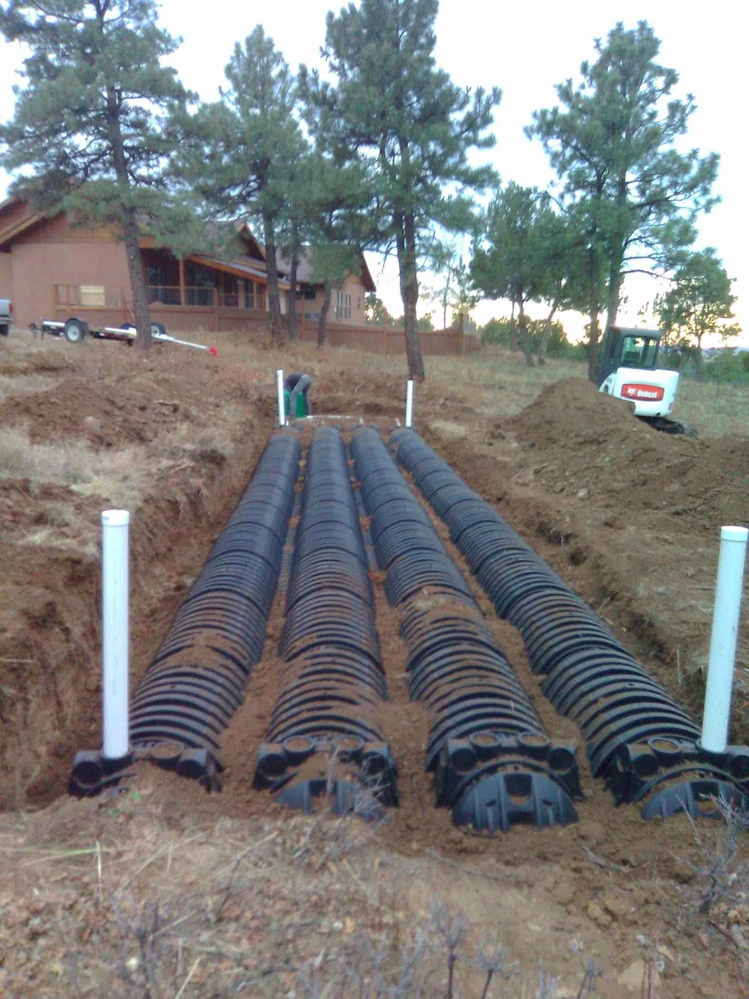 An exposed septic tank system in the dirt ground with a bobcat excavator in the distance.