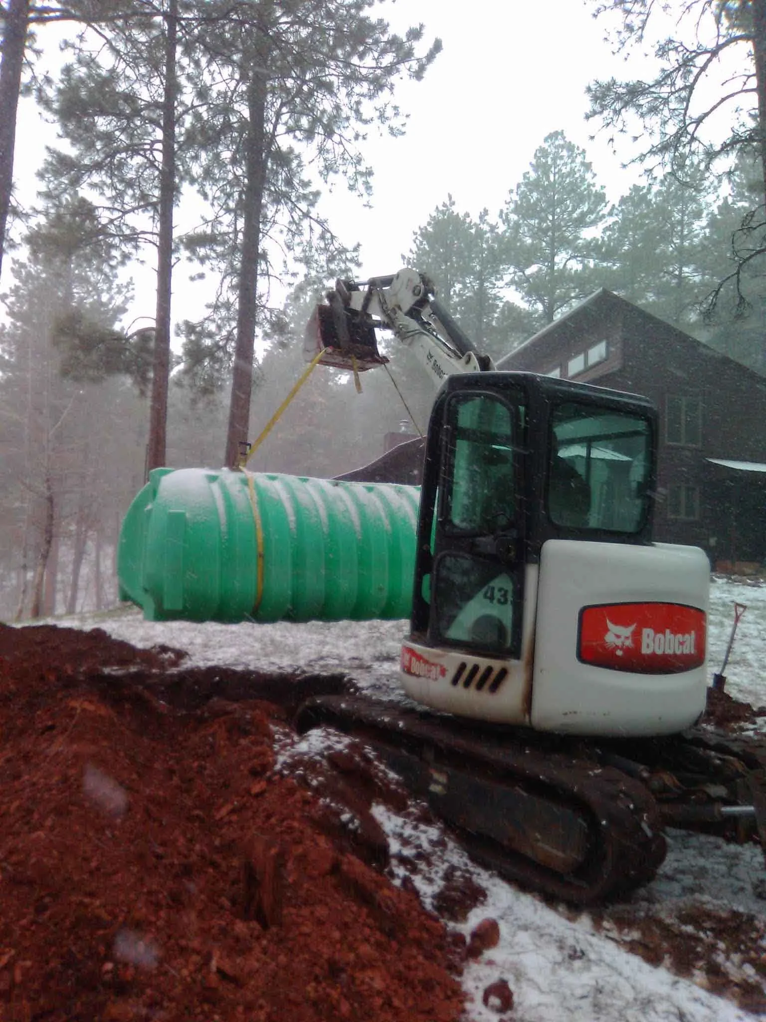 Bobcat Mini Excavator holding a green septic tank. 
