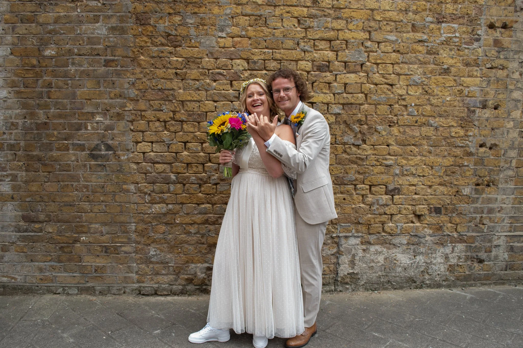 Bride and groom portrait against a brick wall, after their ceremony