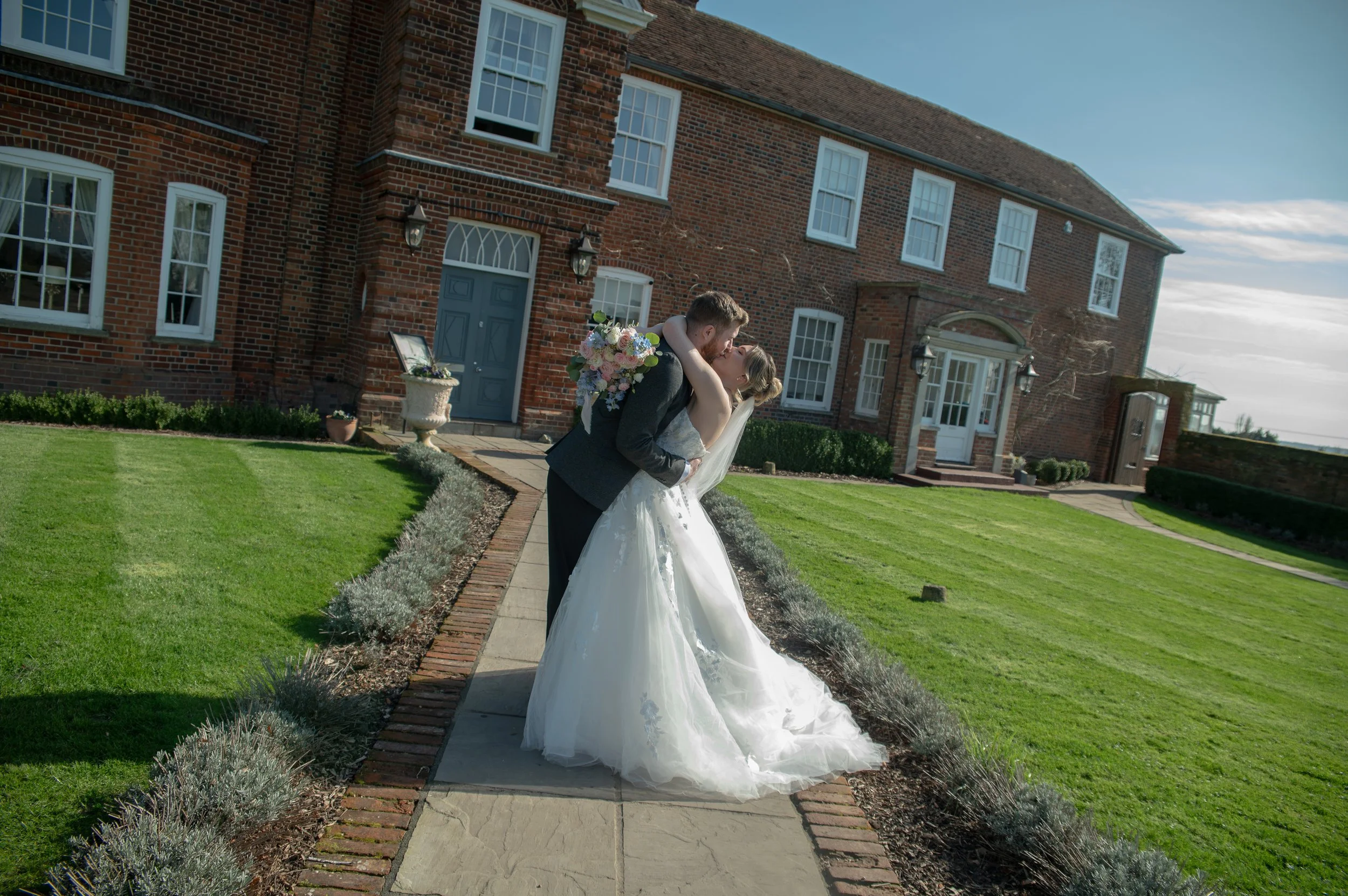 Bride and groom kissing in front of Downham Hall, Essex