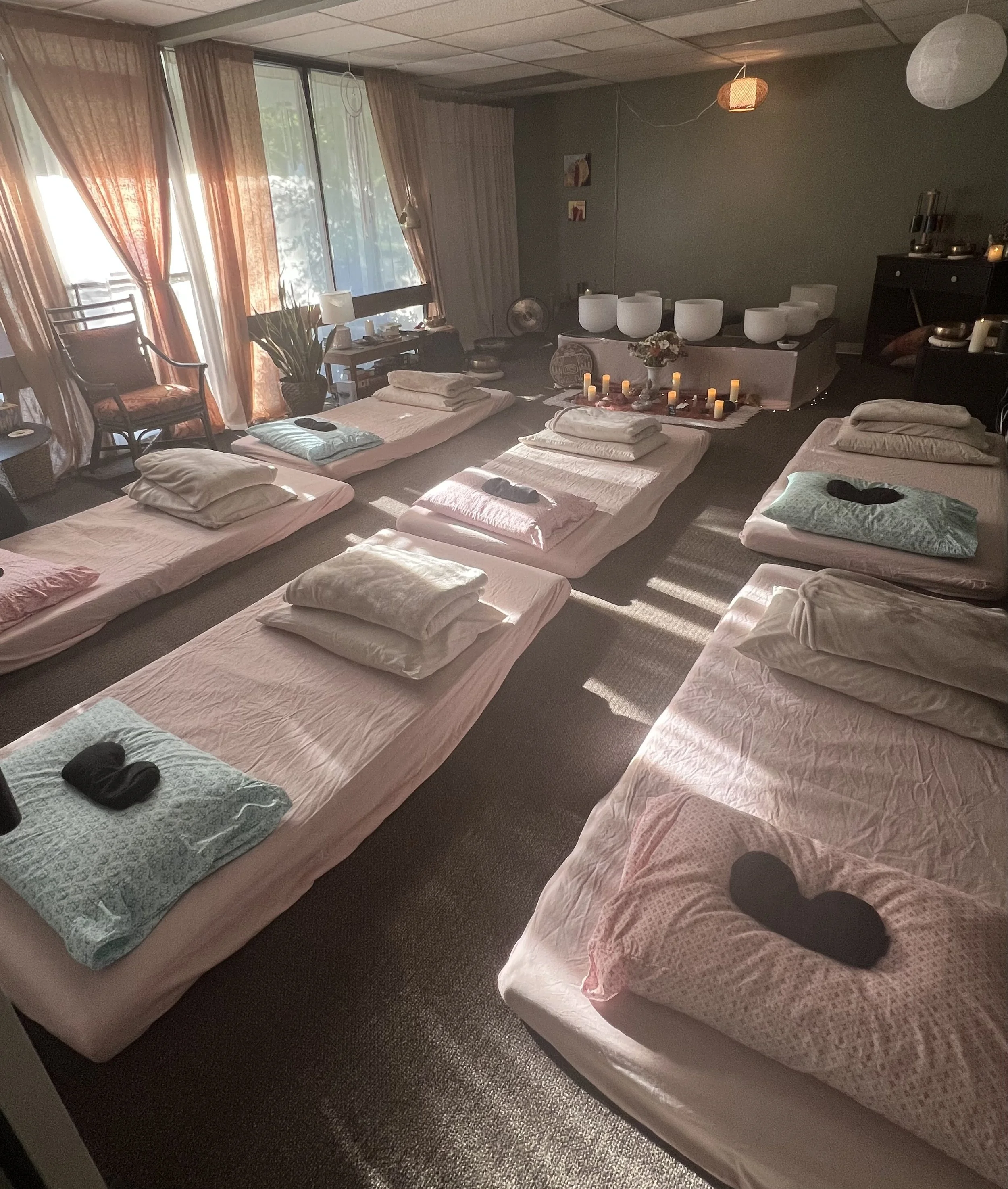 Intimate sound bath space with floor mattresses, blankets, pillows, and soft natural light.
