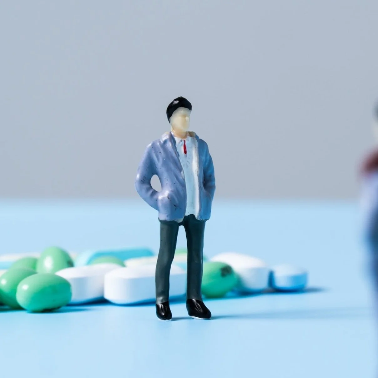 Miniature figurine of a person standing on a blue surface with green and white pills in the background.