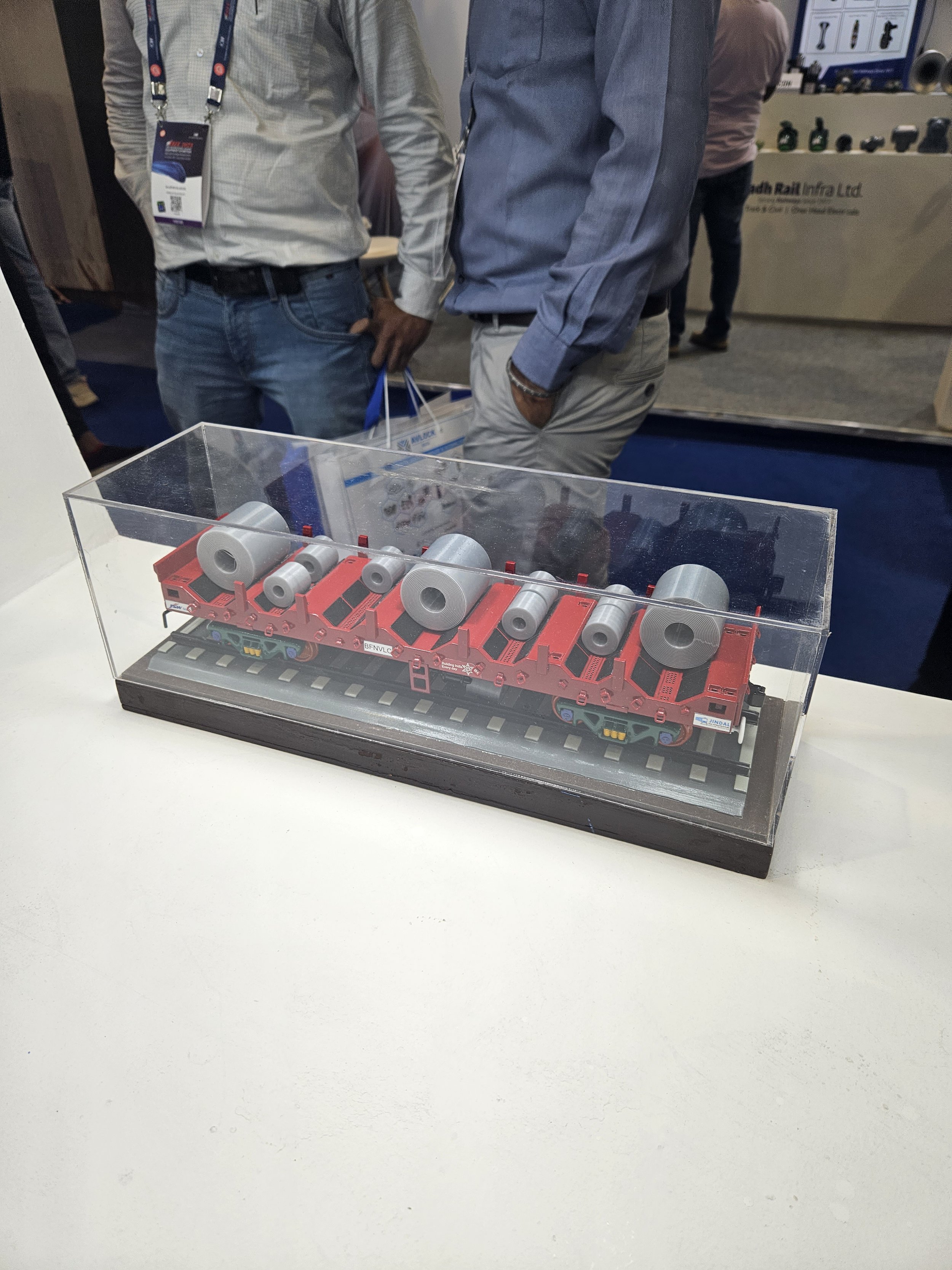 Model train on display in glass case with attendees in background at an exhibition
