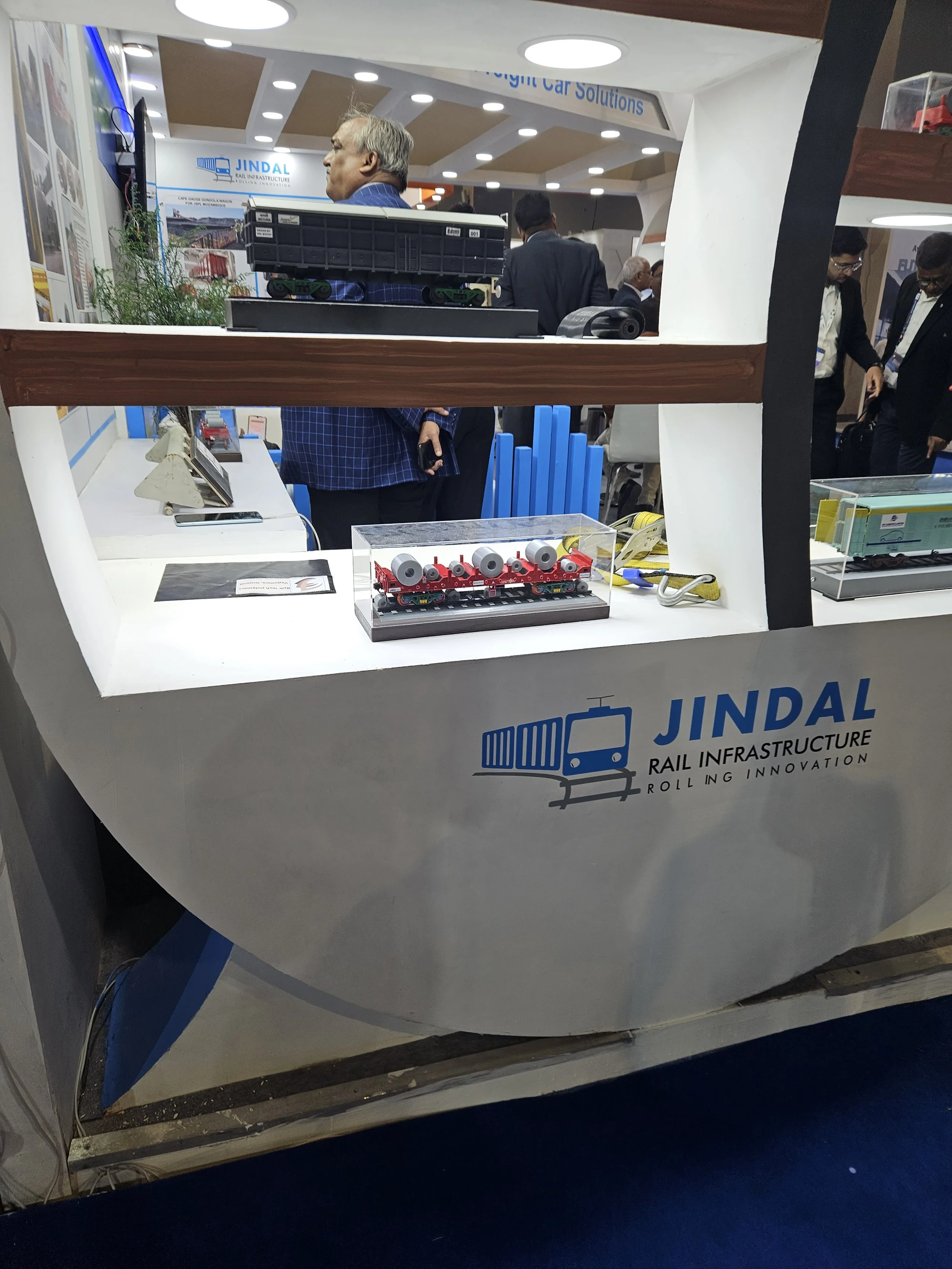 Exhibition booth for Jindal Rail Infrastructure featuring model freight trains and attendees.