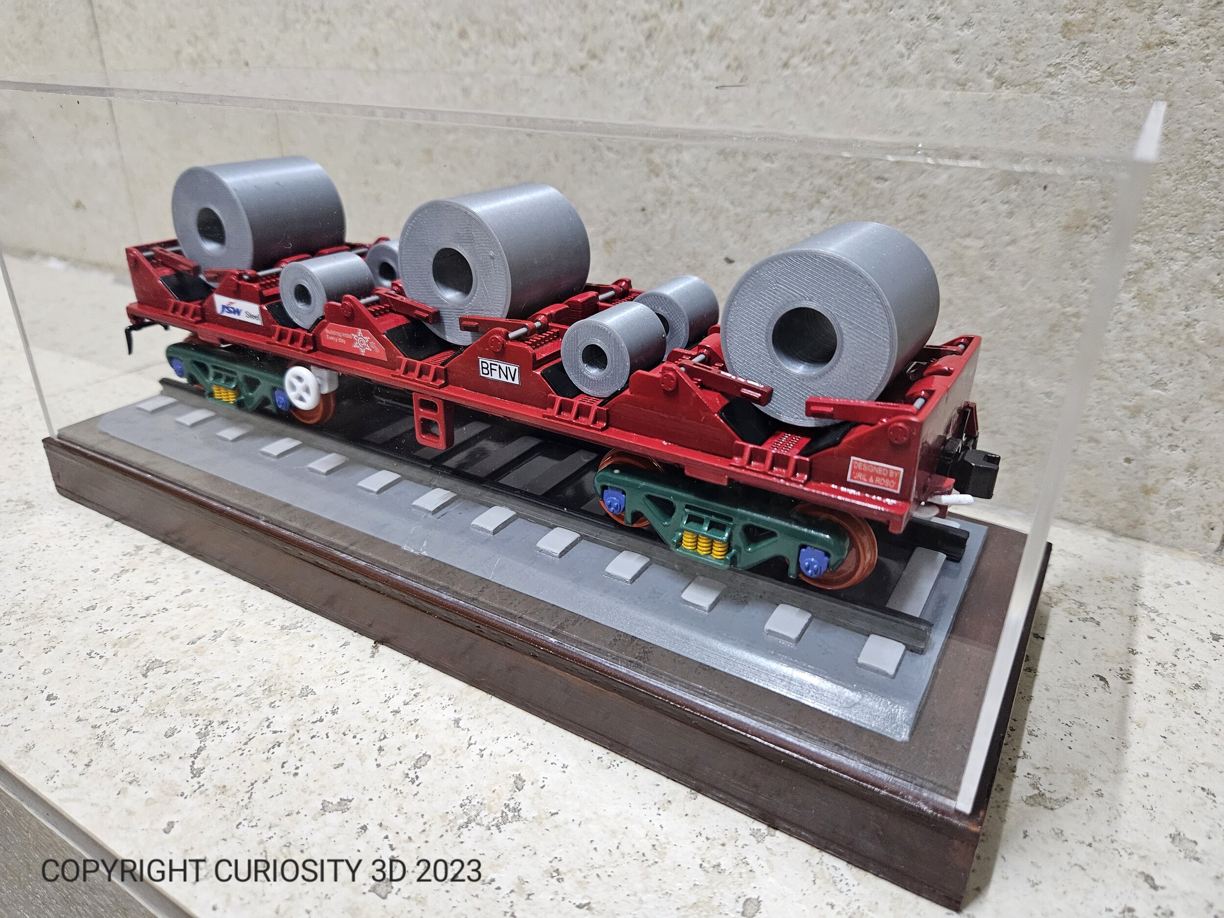 Scale model of a train wagon carrying steel coils, enclosed in a clear display case.