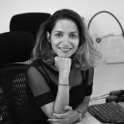 Woman sitting at a desk, smiling, with a laptop and office chair in the background.