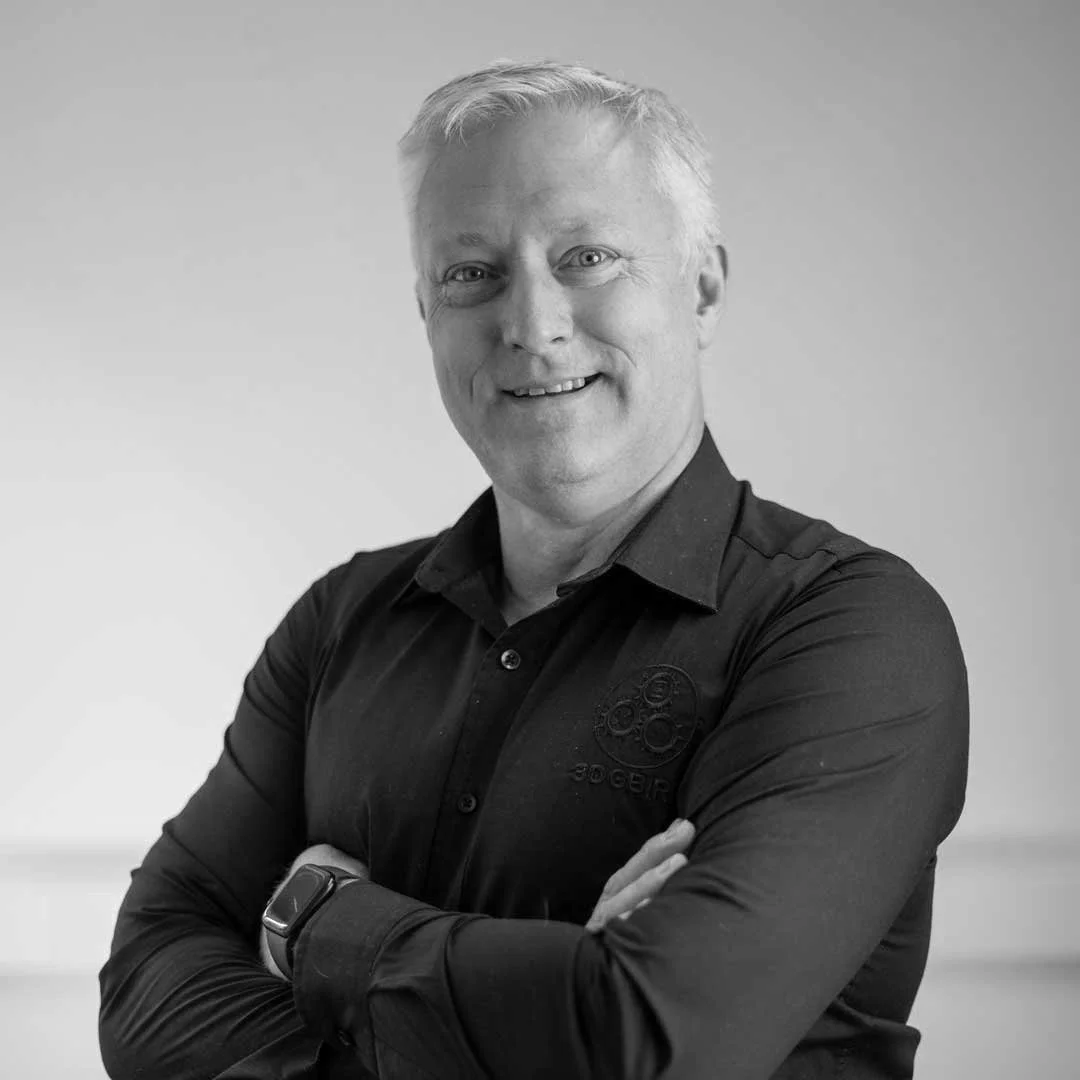 Portrait of a smiling man in a black shirt with arms crossed in a grayscale image.