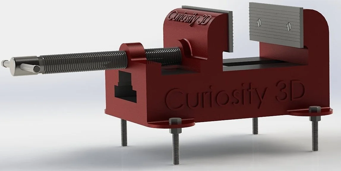 Red metal vise labeled 'Curiosity 3D' with threaded screw and adjustable jaws, mounted on bolts.