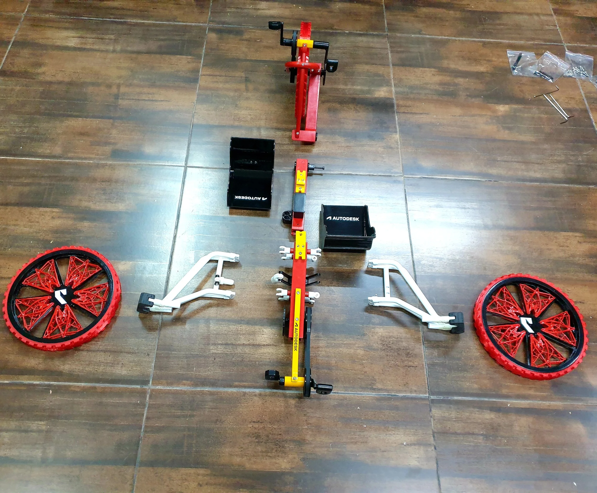 Parts of a buildable bicycle toy with red and black wheels on a wooden floor.