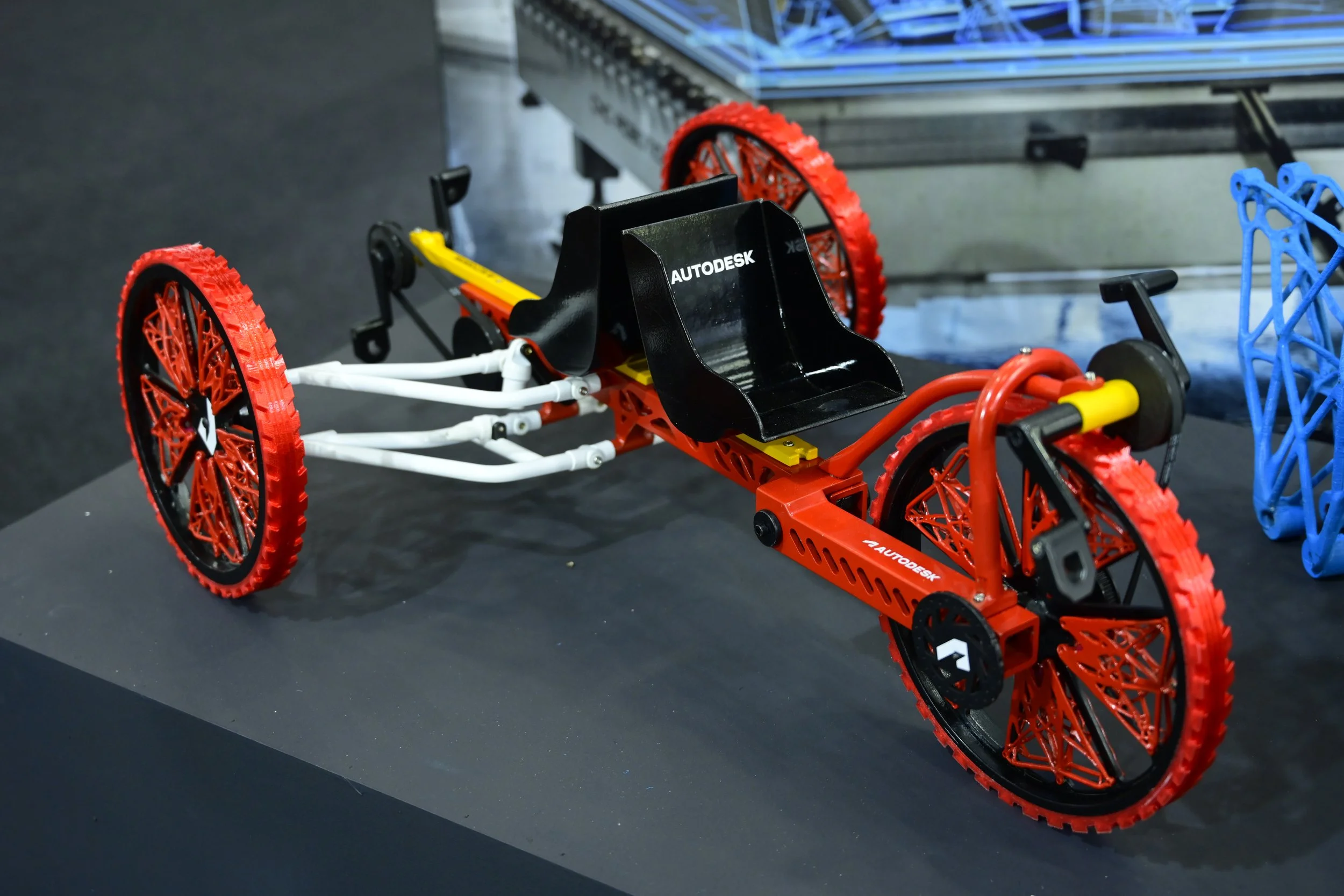 3D-printed tricycle model with red wheels and a black seat displayed on a table.
