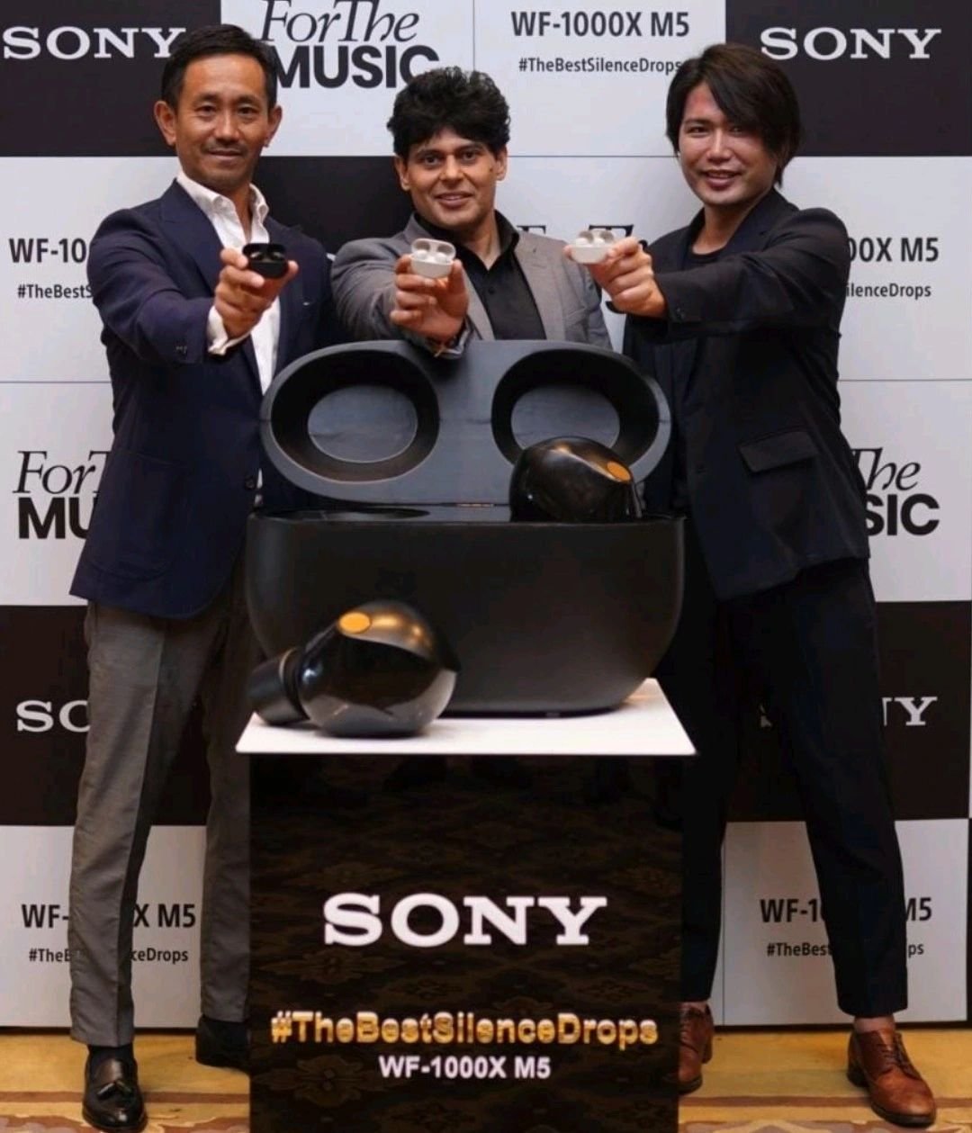 Three men holding Sony WF-1000X M5 earbuds in a promotional event with a large earbud display.