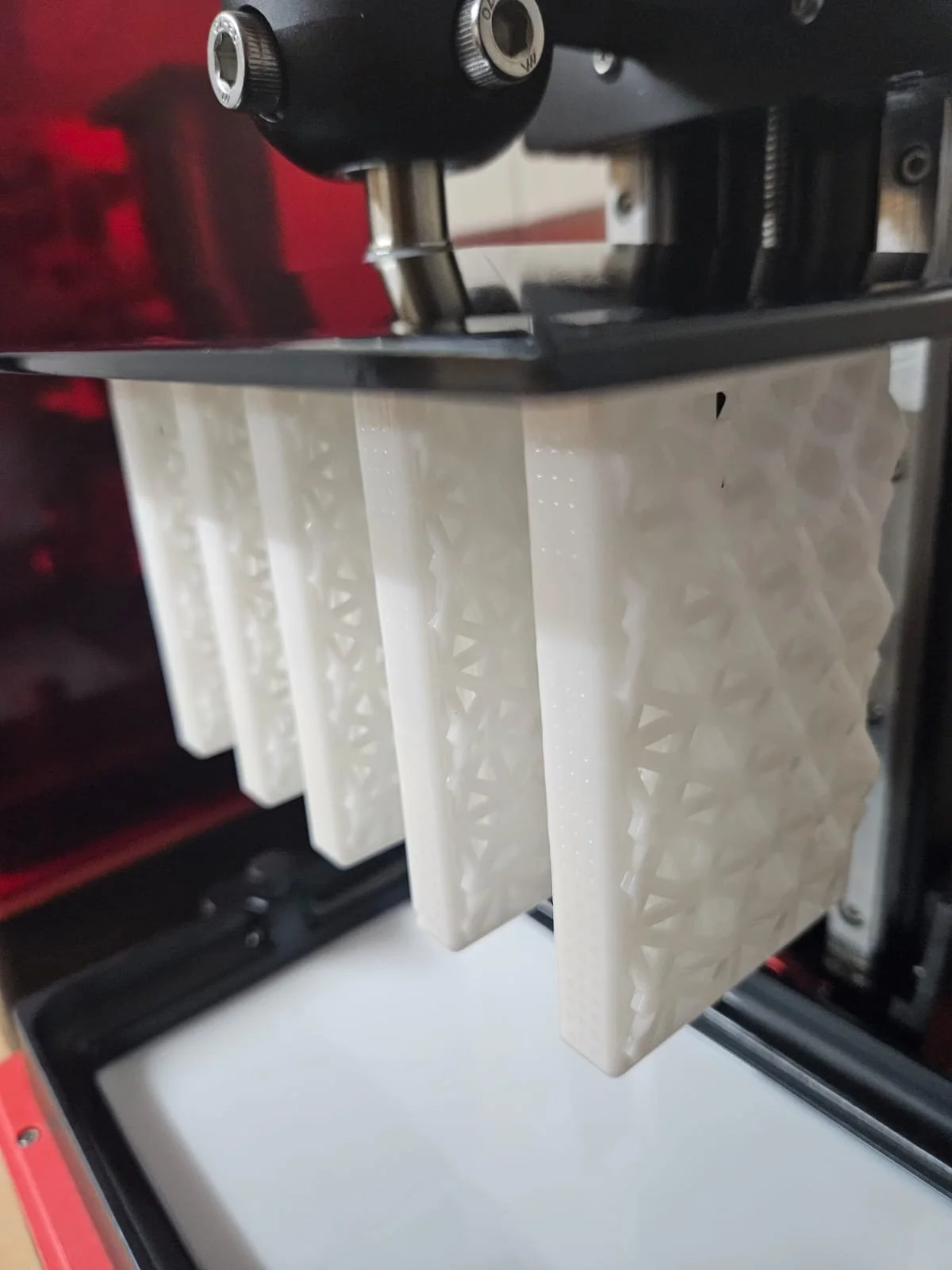 Close-up of a 3D printer with a partially completed print featuring a lattice structure hanging from the build plate.