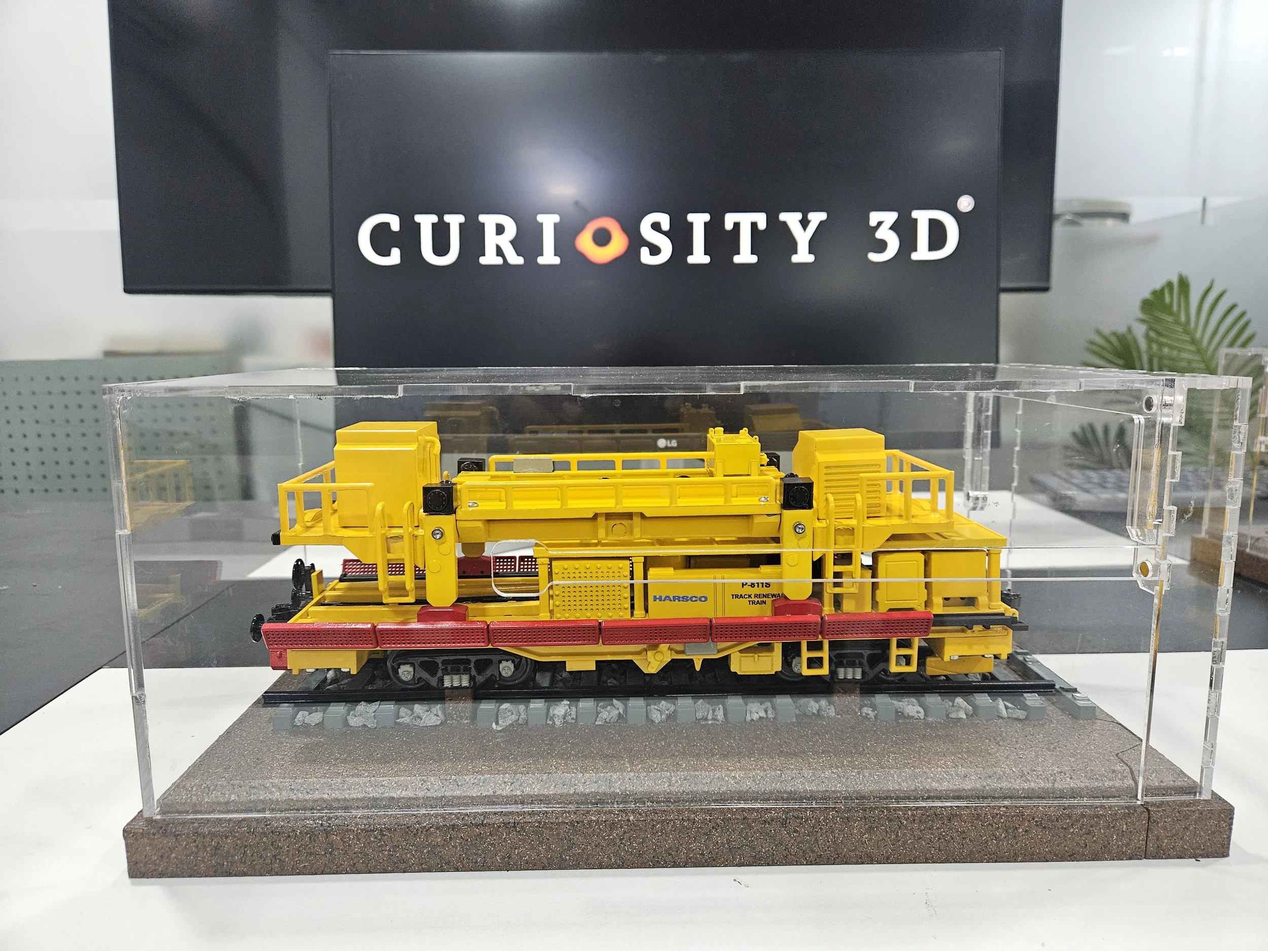 Yellow toy train on display in a glass case with a sign reading "Curiosity 3D" behind it.