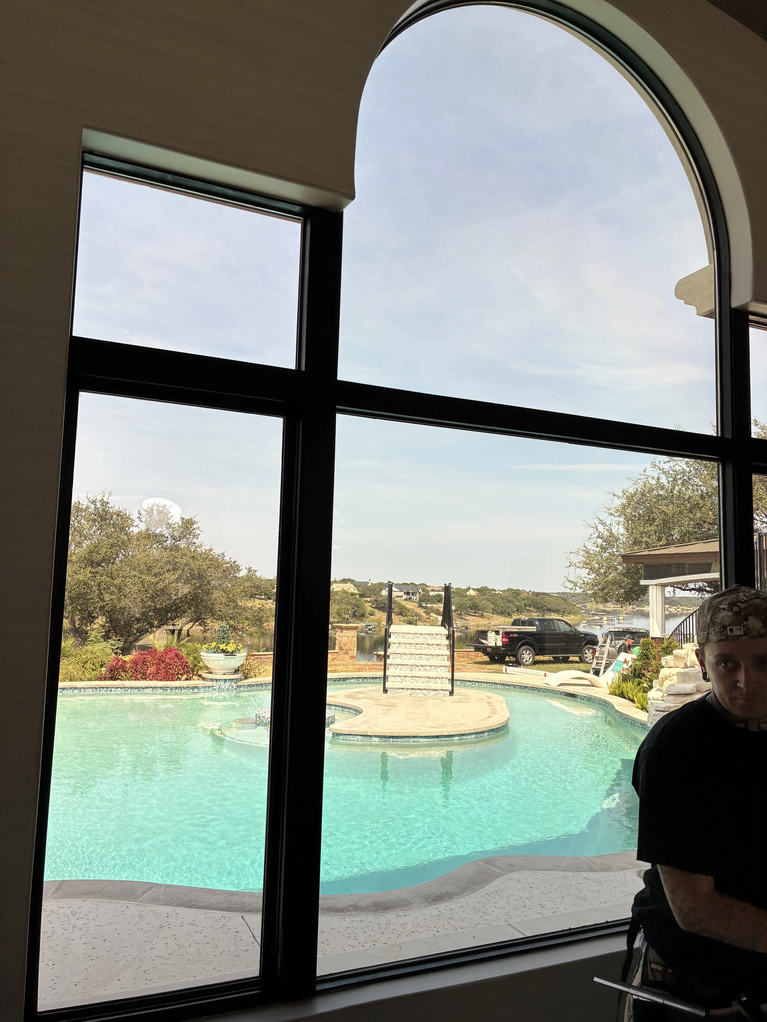 Arched window with solar film overlooking the backyard pool at a lakefront estate