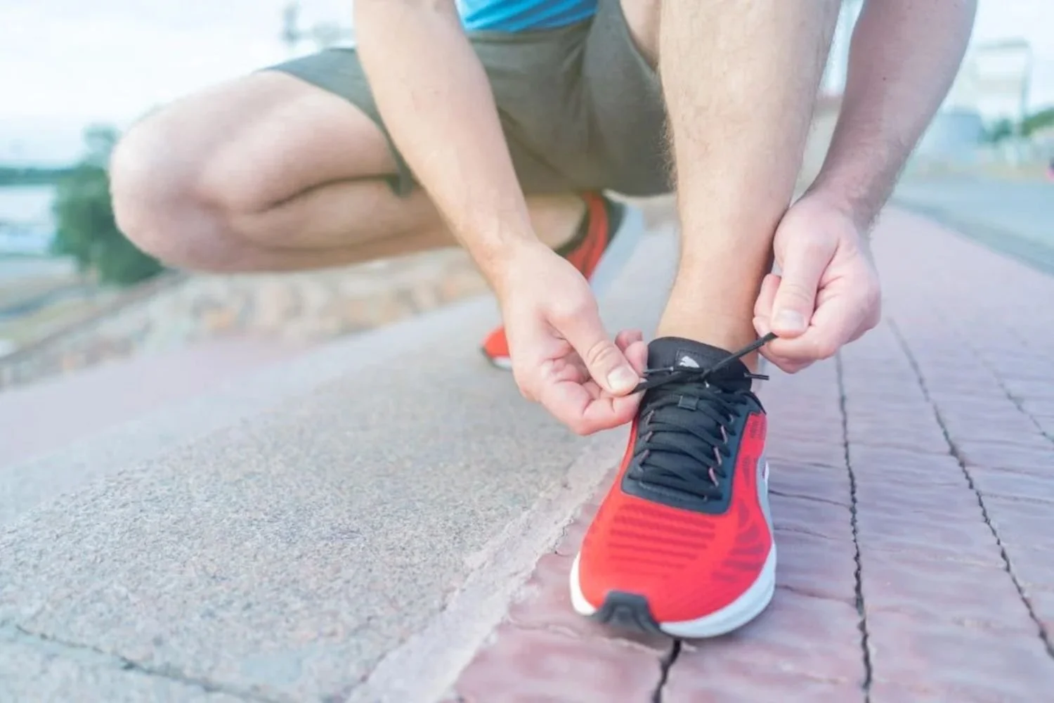 Runner tying running shoes on brick path before a run