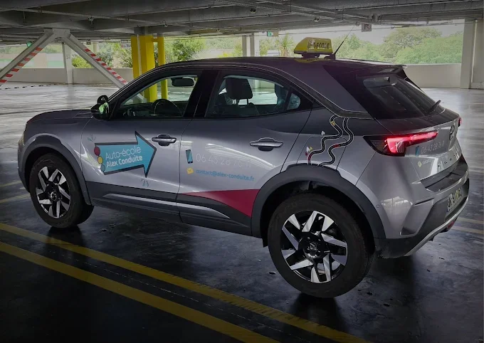Voiture électrique noire et grise avec une publicité pour une école de conduite dans un parking couvert.
