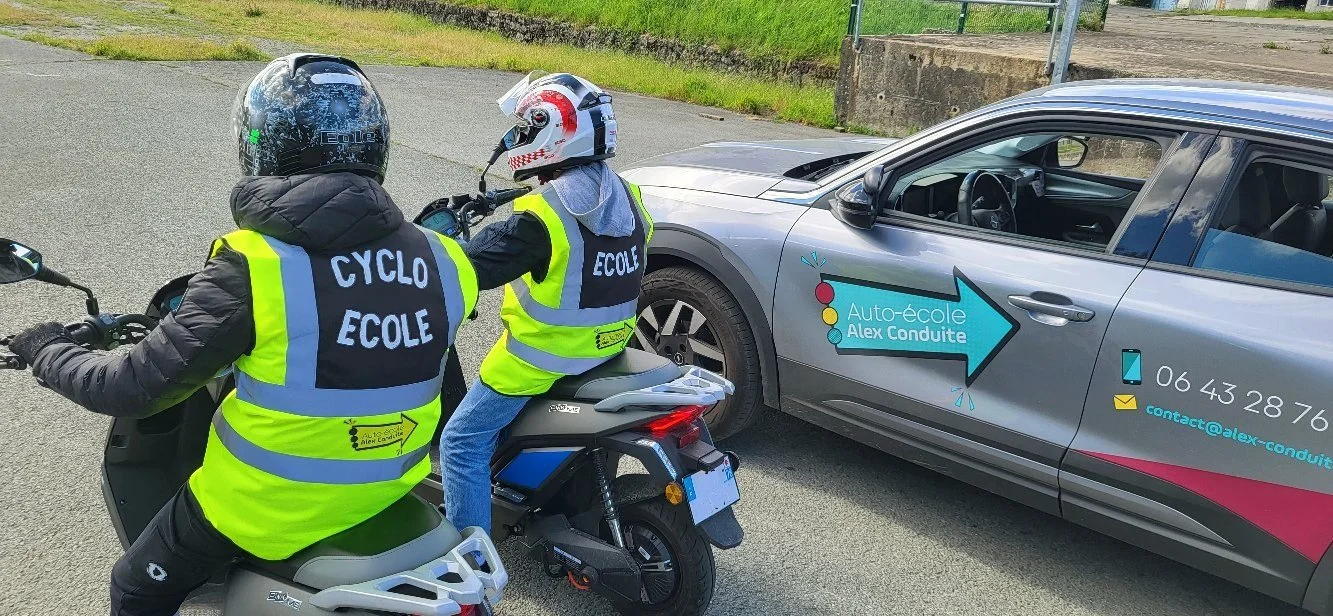 Deux cyclistes portant des vestes fluorescentes avec le texte 'CYCLO ECOLE' échangent avec un conducteur de voiture lors d'une session de formation à la conduite à vélo, devant un véhicule de formation marqué 'Auto-école Alex Conduite'.