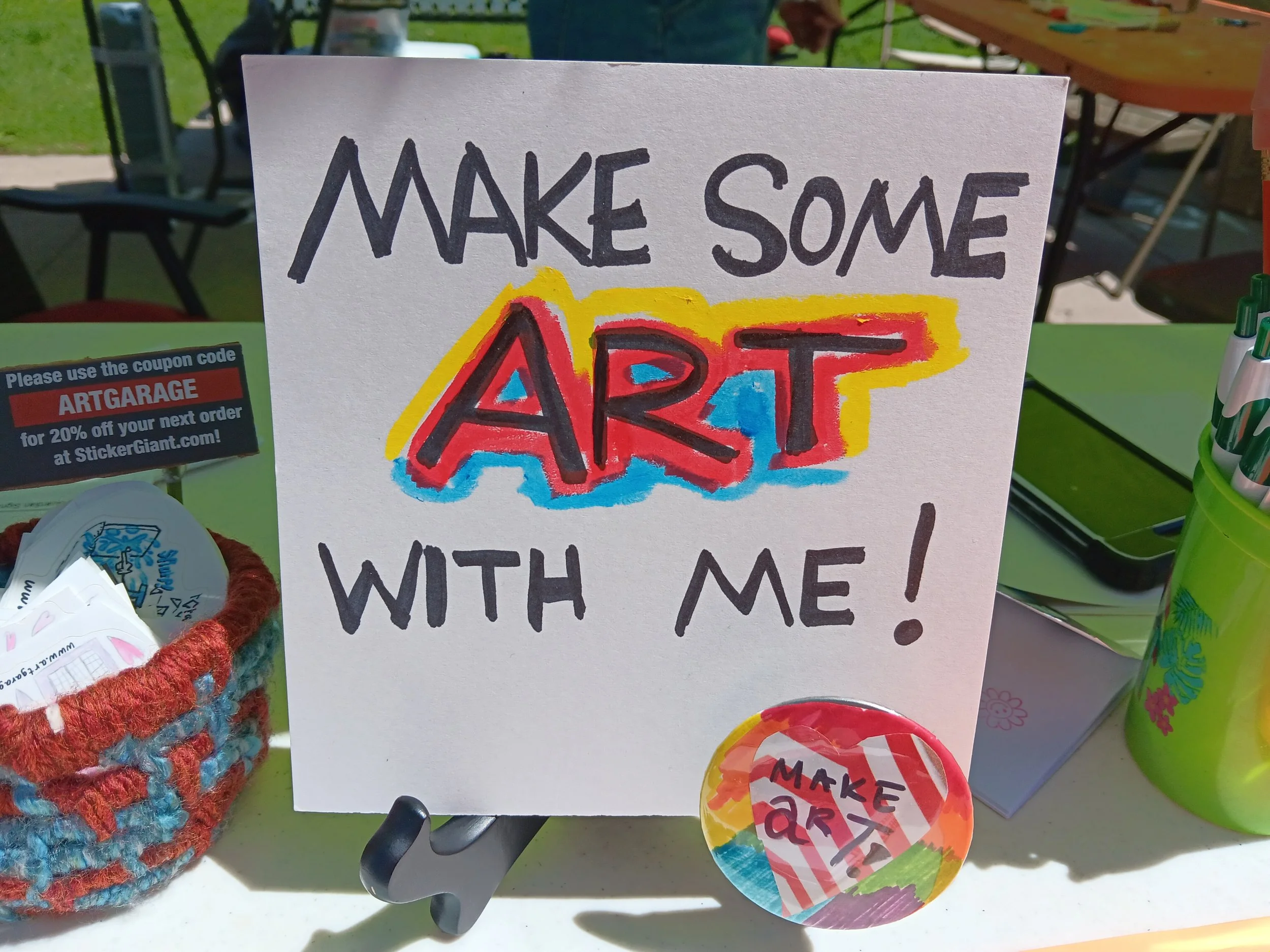Colorful handmade sign reading 'Make Some Art' with a vibrant, graffiti-style 'ART' and artistic surroundings at an outdoor craft fair.