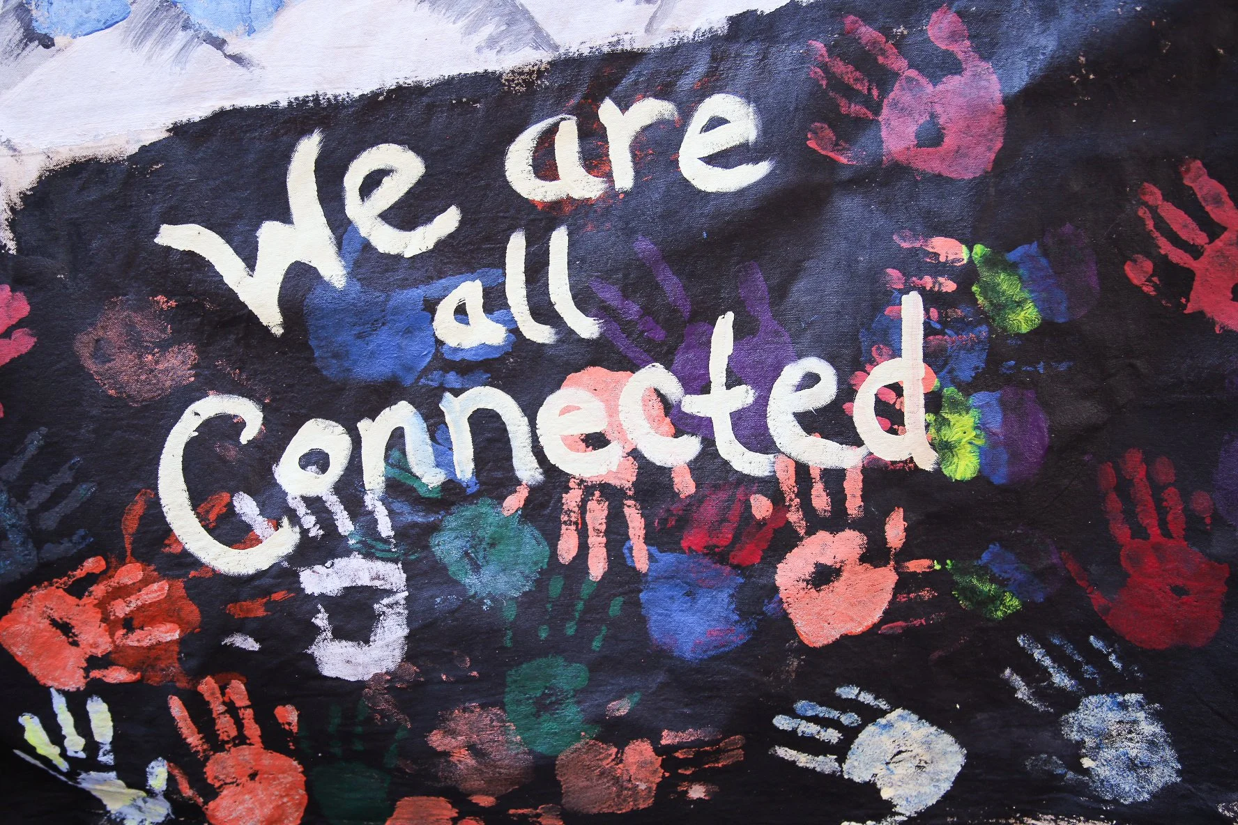 Colorful mural with the phrase "we are all connected" written in white, surrounded by multicolored handprints and paint splatters on a dark background.