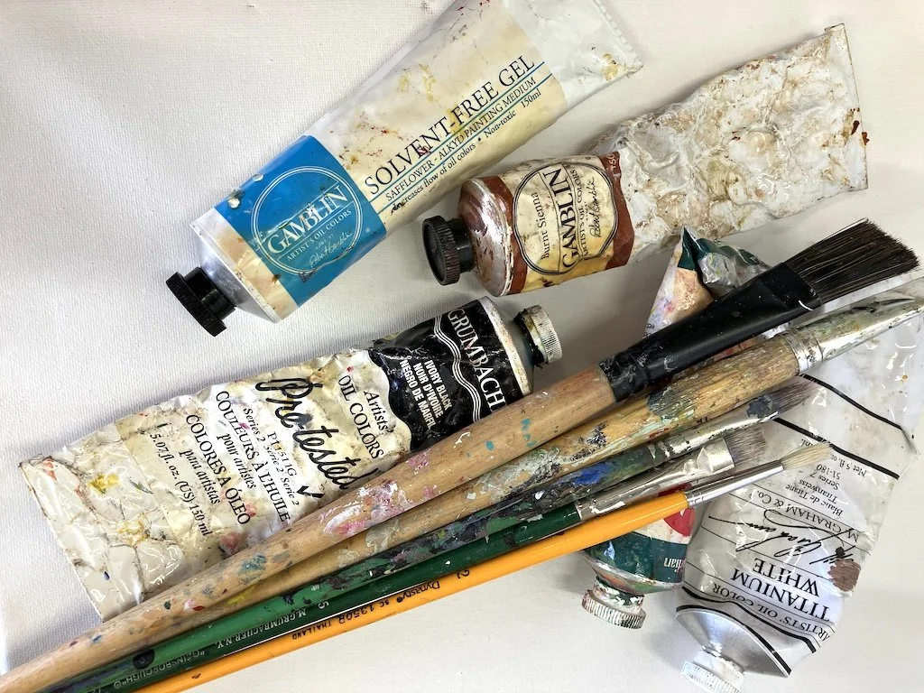 Arrangement of various art supplies including tubes of paint, paintbrushes, and a palette knife.