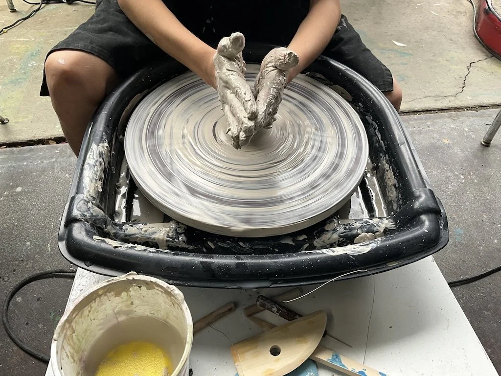 Person shaping clay on a spinning pottery wheel in a workshop.