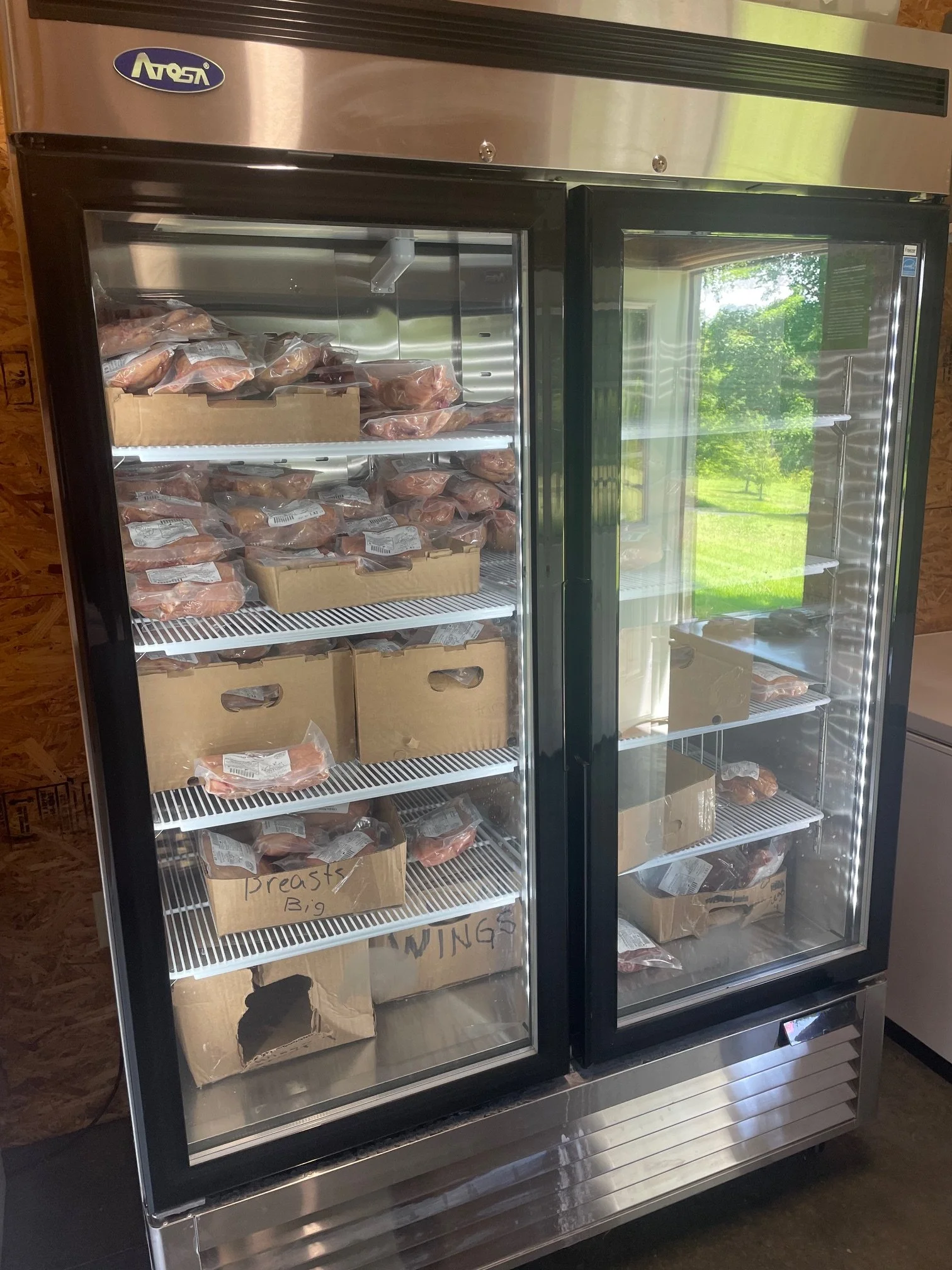 A commercial refrigerator filled with packages of raw chicken and cardboard boxes labeled 'Breasts'.