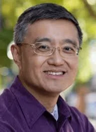 Portrait of a smiling man with glasses, wearing a purple shirt outdoors
