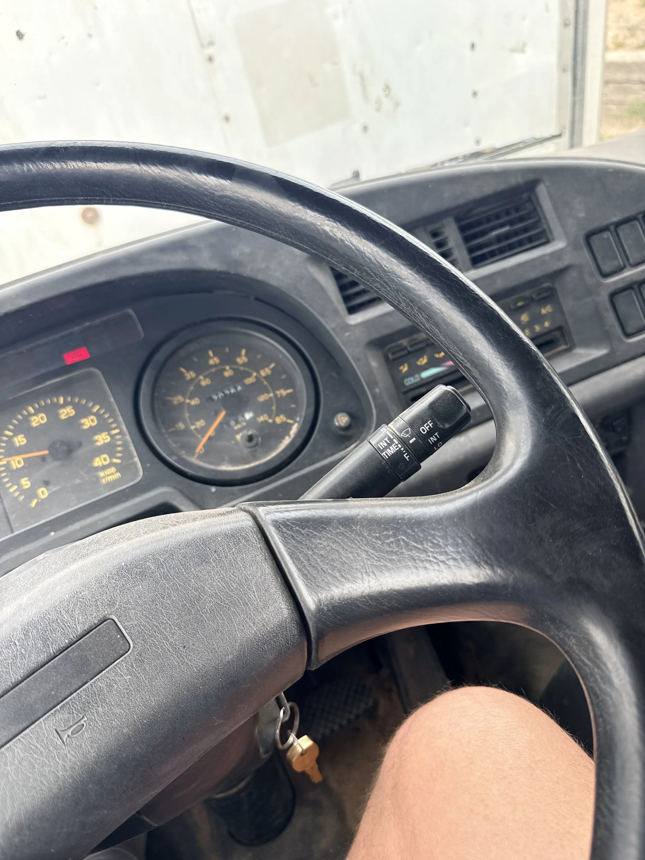 Inside a vehicle, looking from the driver's seat towards the dashboard and steering wheel, with part of a person's knee and leg visible.
