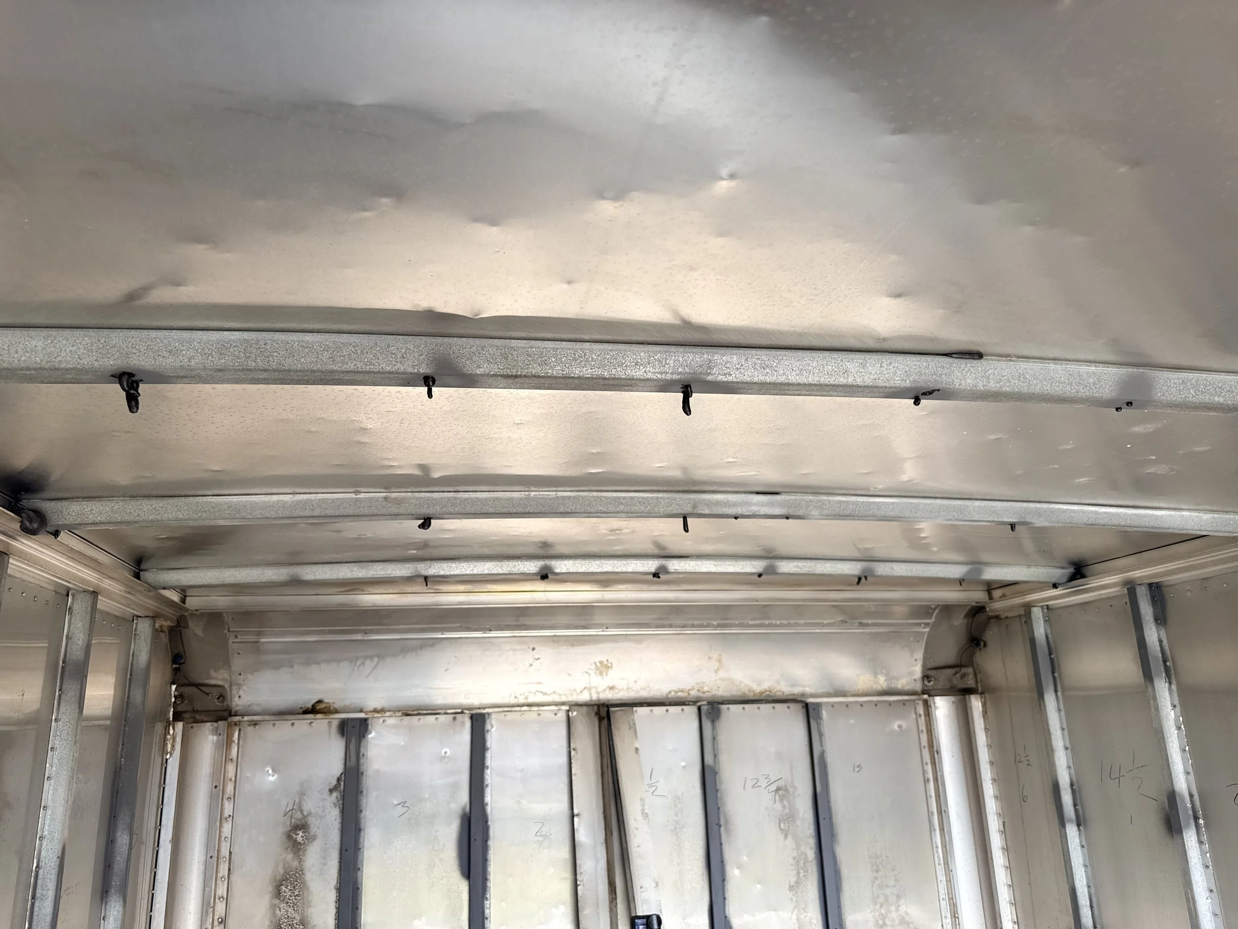 The interior of a metallic structure, possibly an elevator shaft or duct, with metal beams and some handwritten notes or measurements on the walls. There are small screws or fasteners on the beams, and the area appears unfinished or under constructio