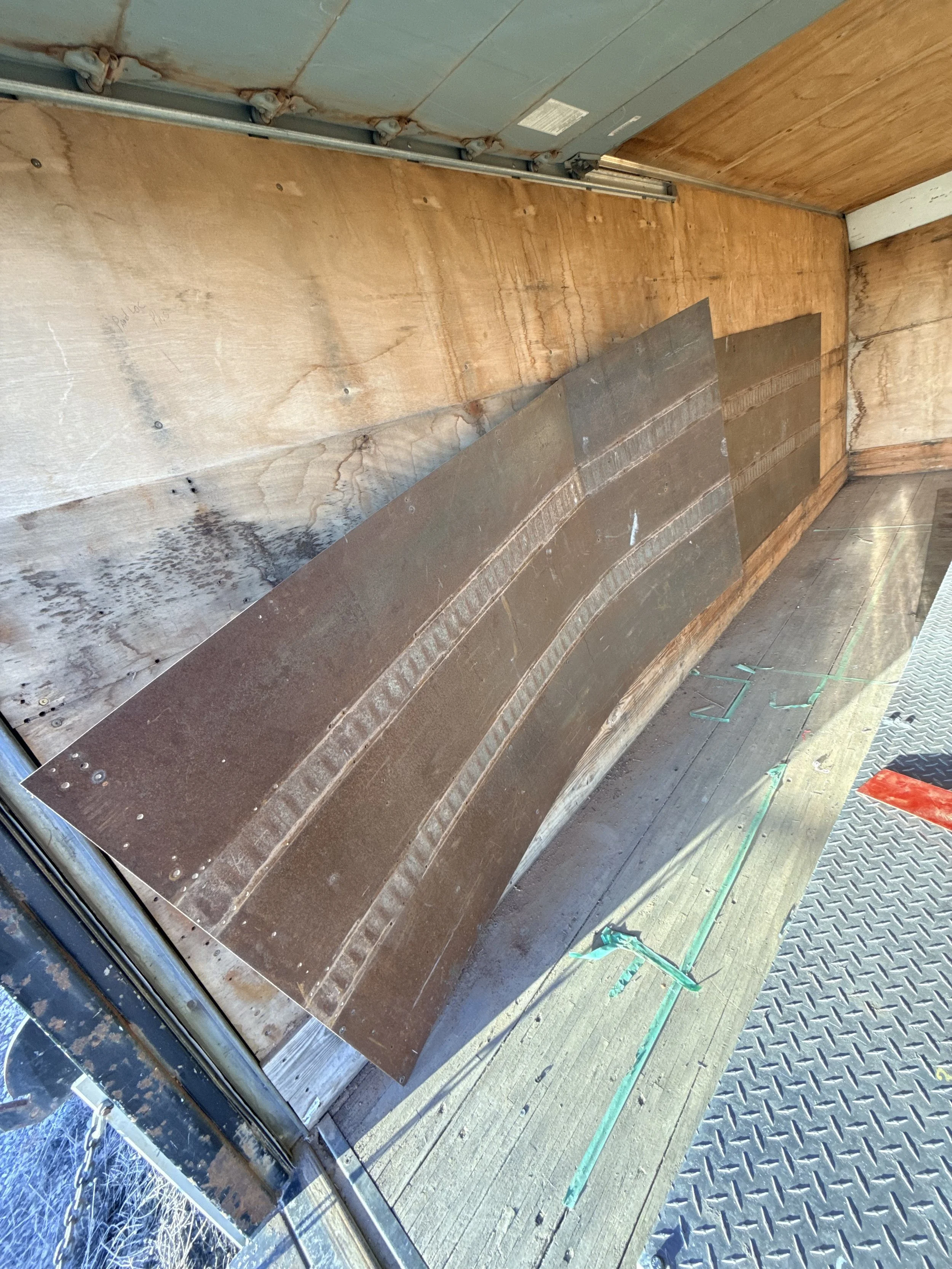 Close-up of a construction or renovation project showing a curved section of metal panels and wooden wall with electrical wiring and pipes on the ceiling.