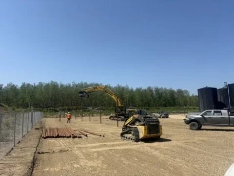 Construction site with a small excavator, workers, and parked vehicles under a clear blue sky.