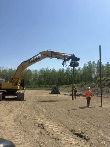 Construction workers using a crane to install a utility pole at a job site with a clear blue sky.