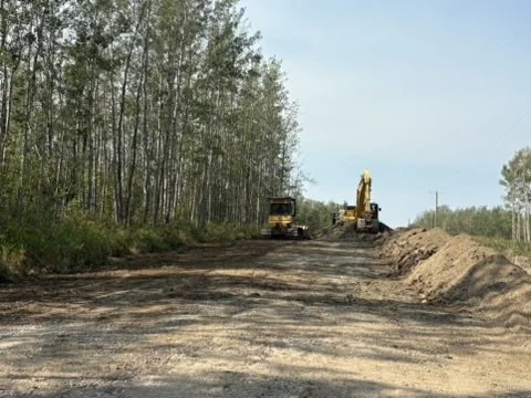 Construction site with bulldozer and excavator on dirt road with trees in the background.