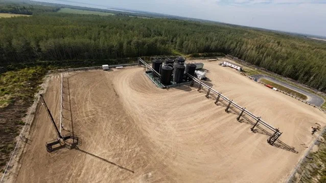 Aerial view of an oil or gas extraction facility surrounded by trees and open land.