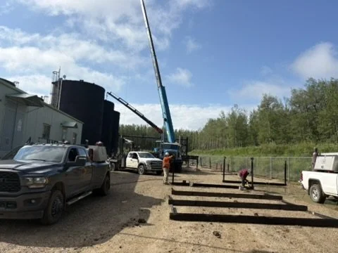 Construction workers installing wooden beams on a building site with trucks and a crane under a blue sky.