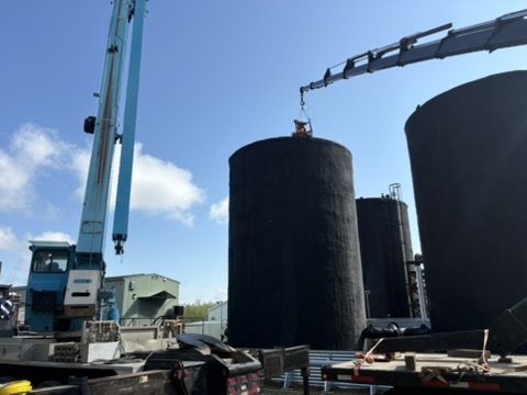 A crane lifting a large cylindrical tank at an industrial construction site.