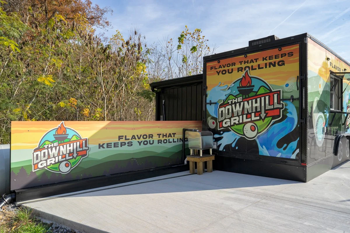 A food truck named 'The Downhill Grille' with a colorful mountain landscape and water design on the sides and slogan 'Flavor That Keeps You Rolling.' Smokies Design creative team providing graphic design, branding, website design, and marketing servi