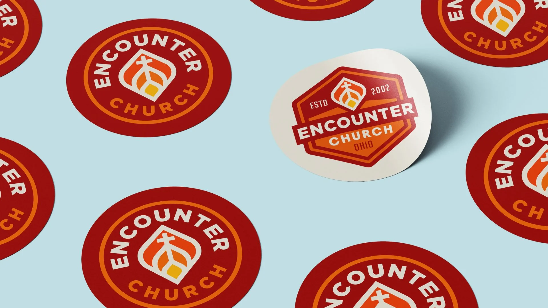 A collection of stickers featuring a church logo that says 'Encounter Church Ohio' with an established date of 2002, arranged on a light blue background. sticker design East Tennessee, rack card design and printing in pigeon forge, Custom logo design