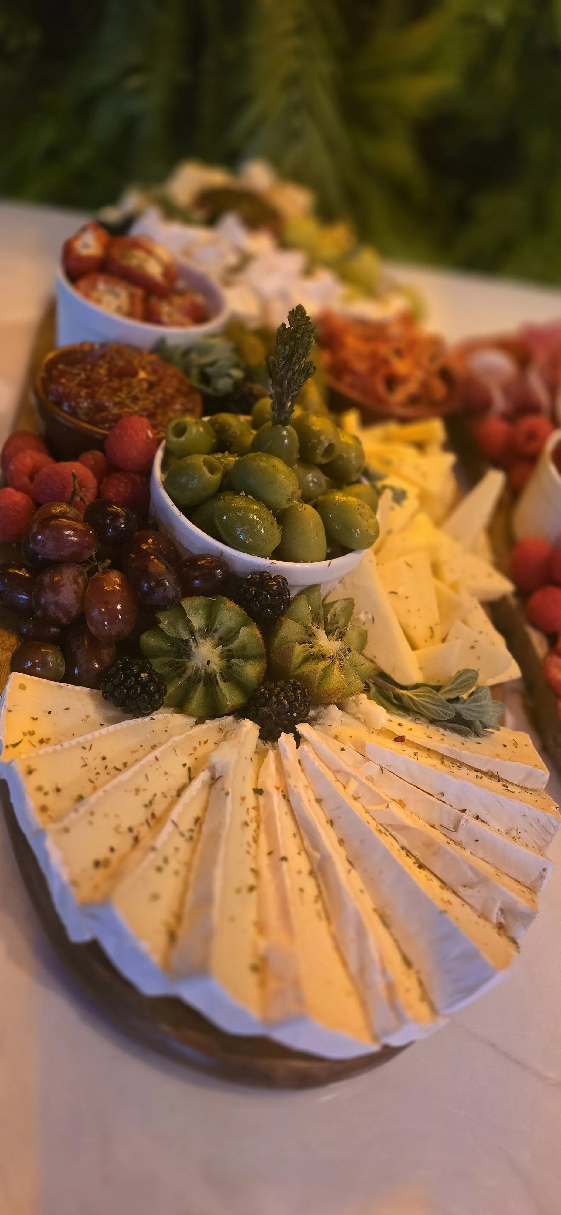 A cheese platter with sliced cheese, green olives, grapes, kiwi, blackberries, and raspberries, garnished with herbs. A premium offering at ninety seven bar Sidcup Kent.