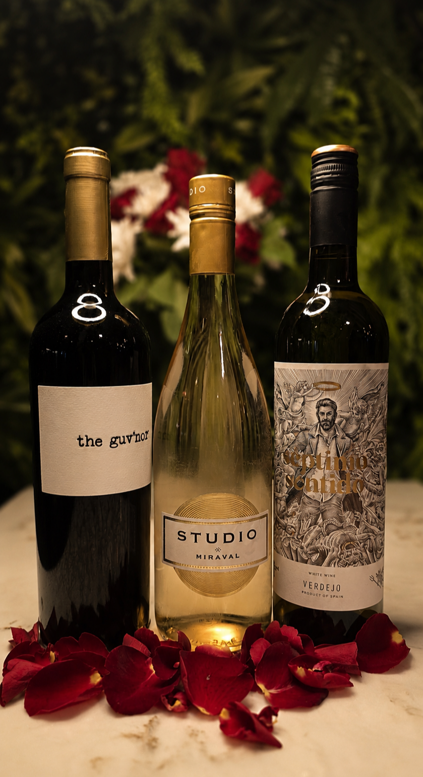Three bottles of premium wine on a marble bar, surrounded by red rose petals, with a green leafy background and red and white flowers in the distance. 97 Wine Bar in Sidcup Kent.
