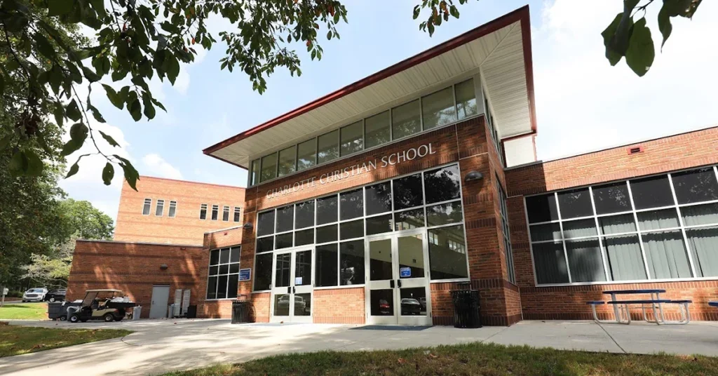 Exterior view of Charlotte Christian School with brick facade, large windows, and glass entrance doors, surrounded by trees and a sidewalk.