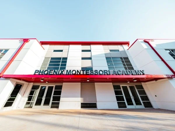 Front view of Phoenix Montessori Academy building with modern white exterior, red trim, and large windows.
