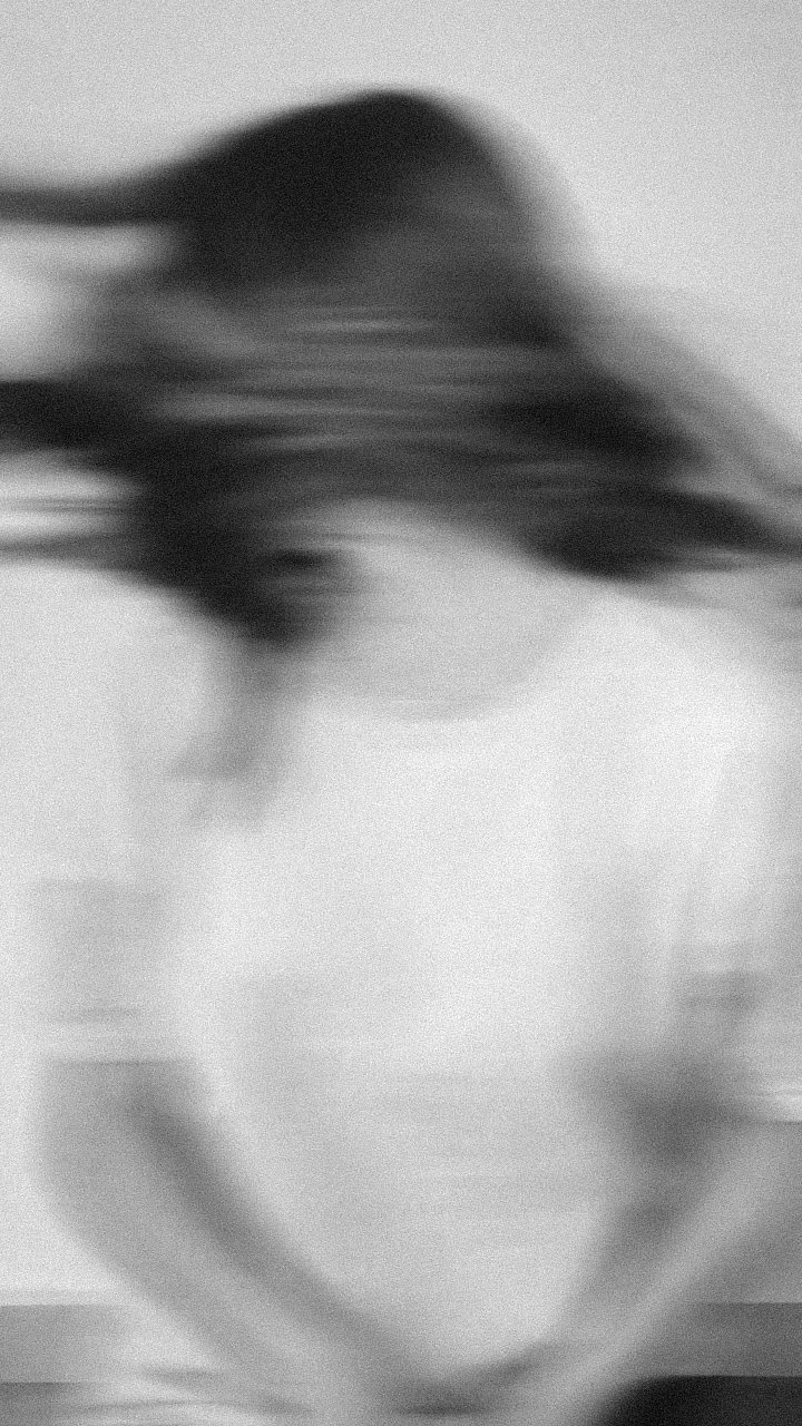A blurred, black-and-white close-up of a person's face with their eyes closed and hair flowing.