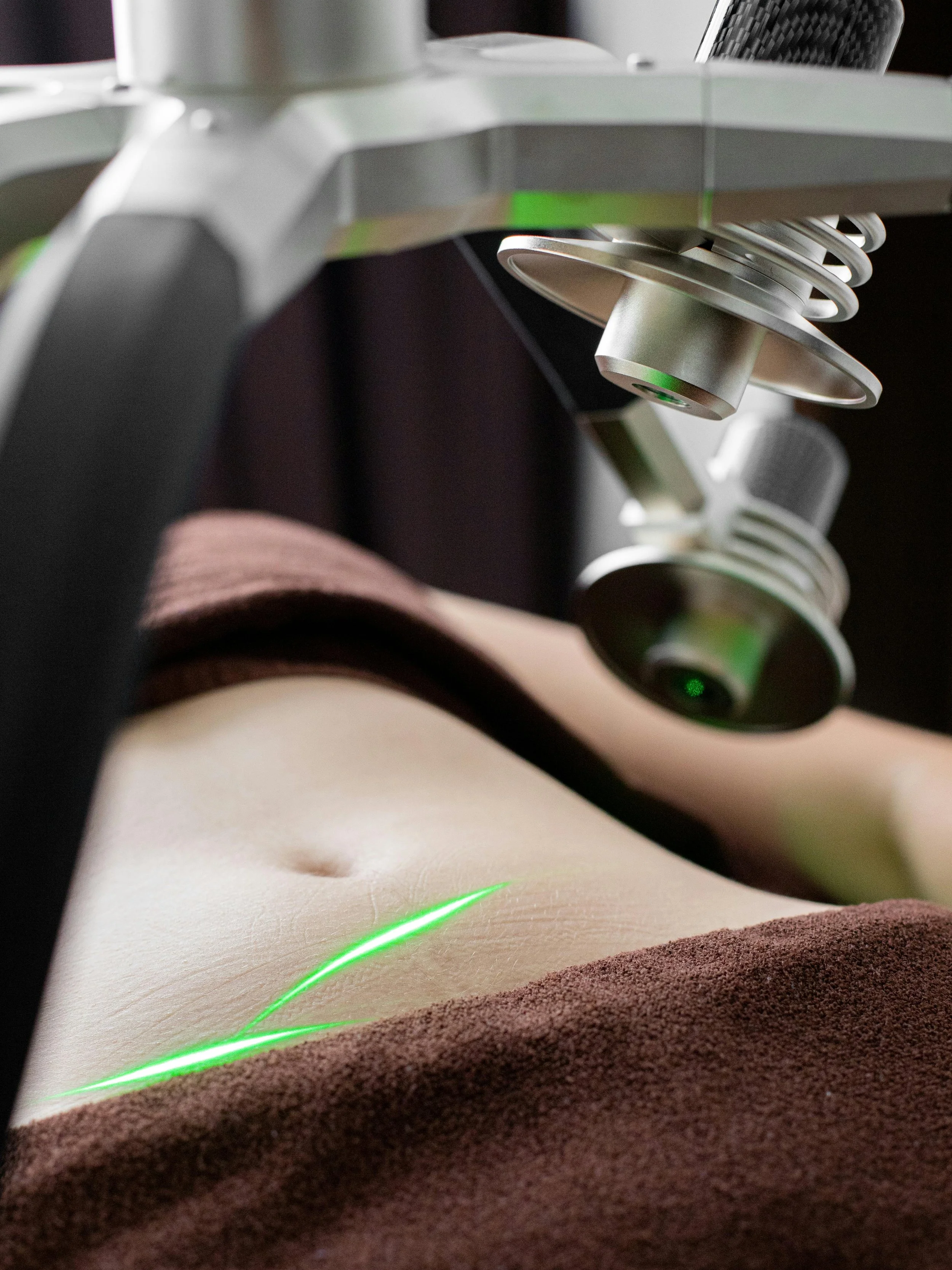Close-up of a microscope focusing on a skin sample with a green laser beam visible on the surface.