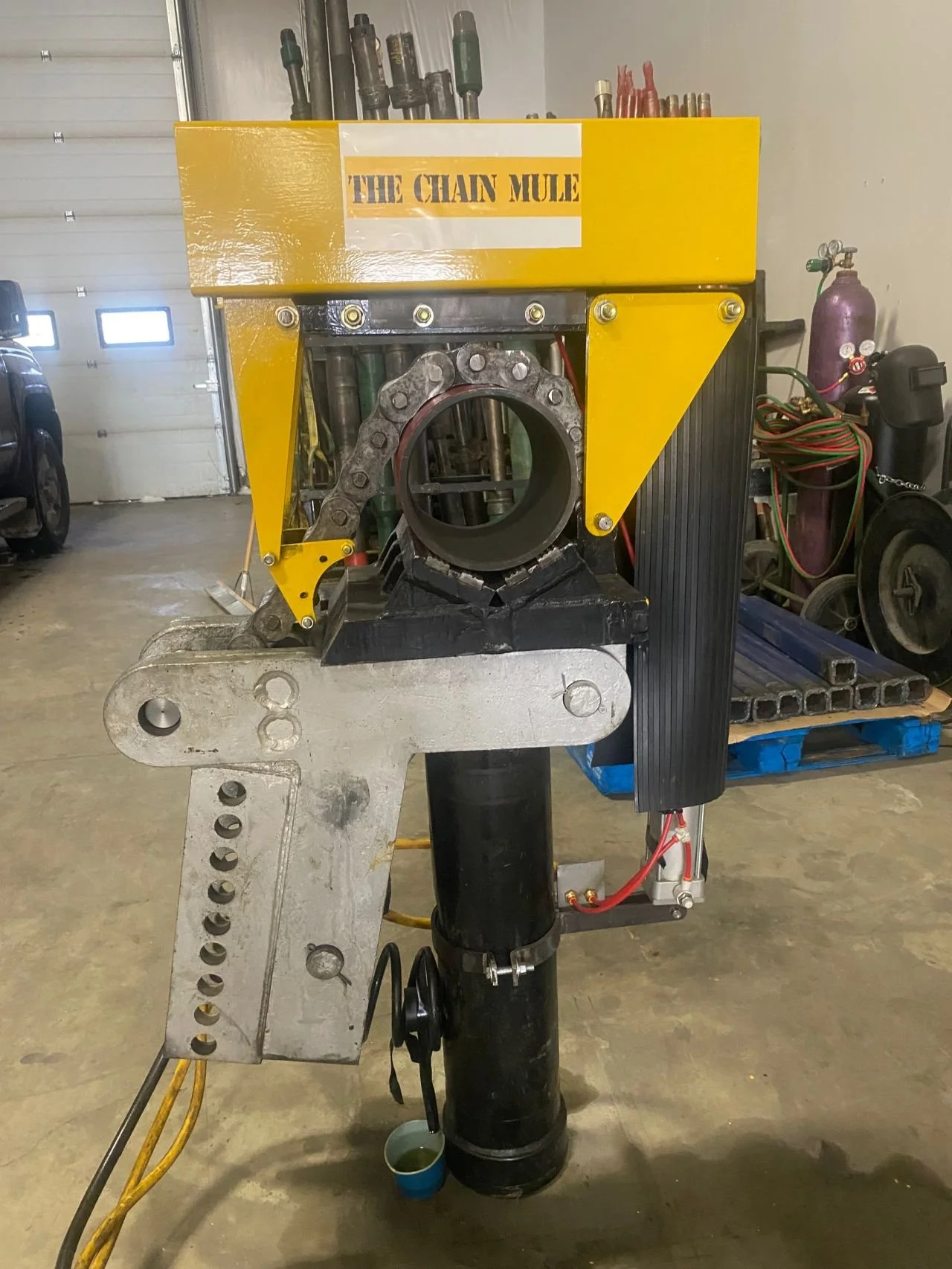 A mechanical device labeled 'The Chain Mule' with a yellow top, metal chain, and various components in a workshop setting.