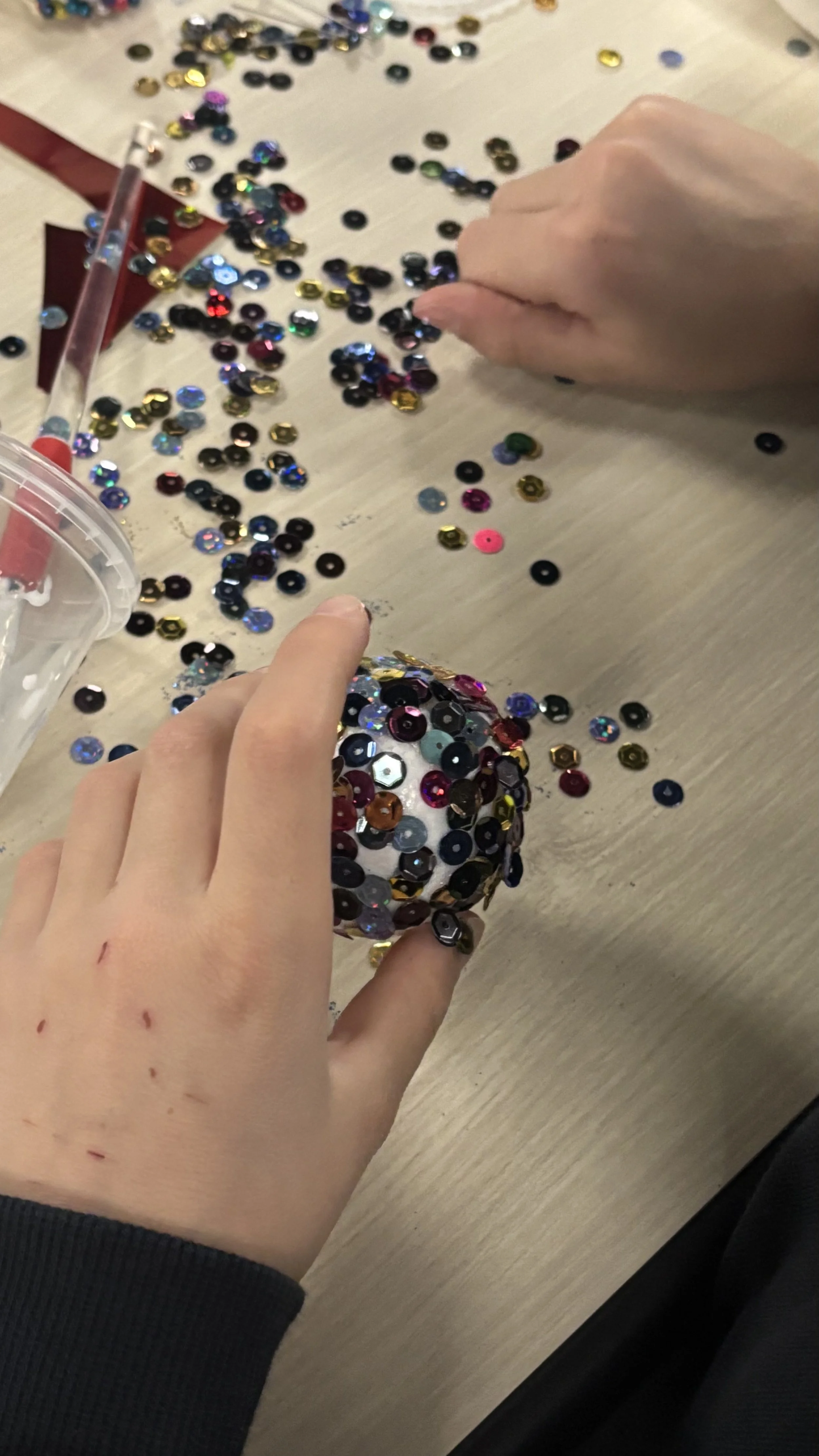 People decorating a Christmas ornament with colorful sequins at a table.