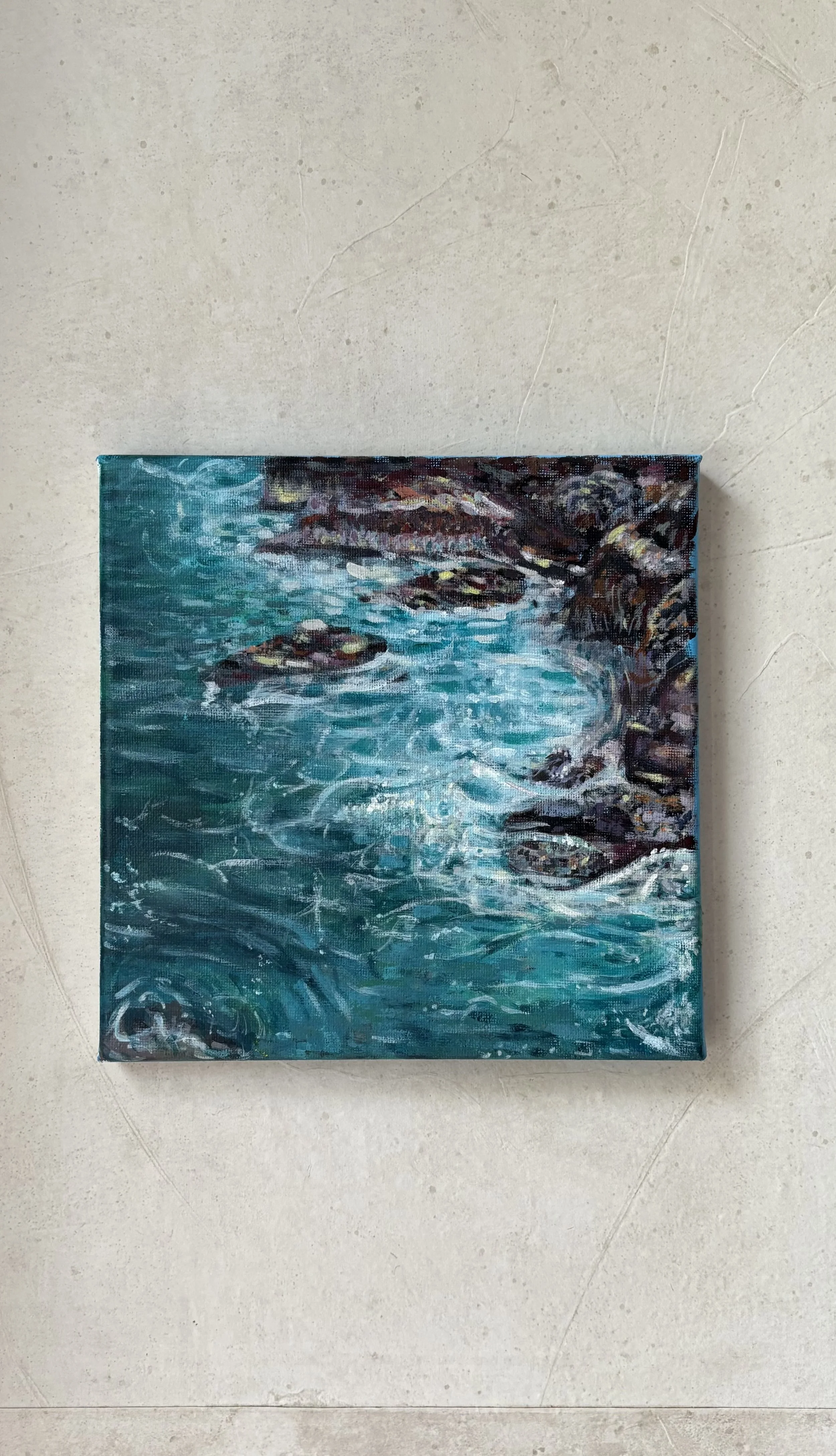 Part of a painting of water with rocks on the edge, displayed on a light-colored tiled floor.
