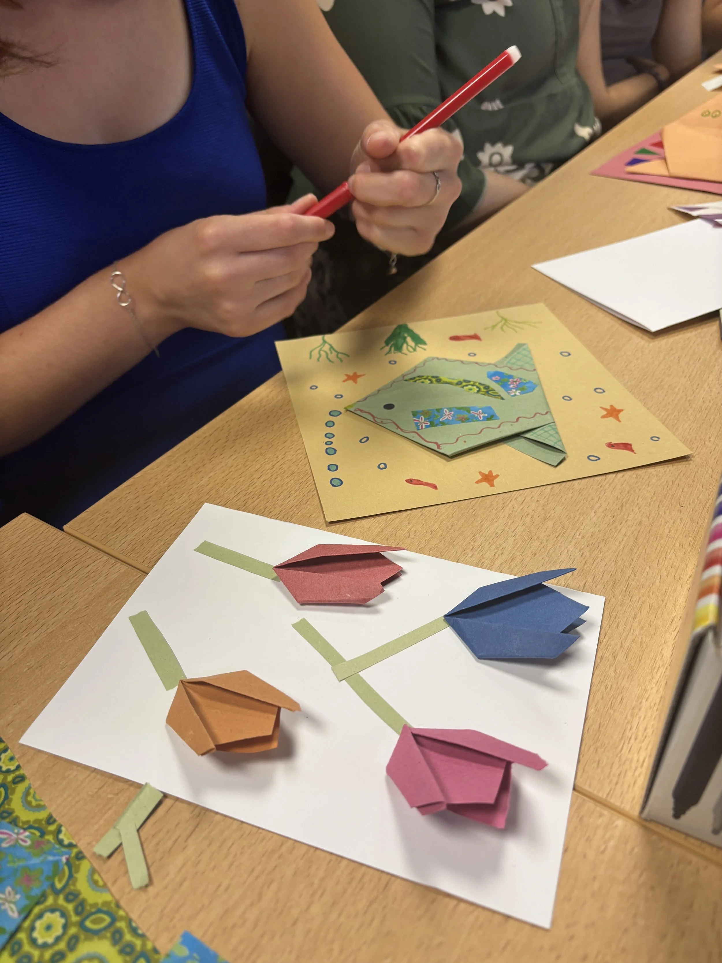 People creating origami animals on a wooden table with colored paper and instructional sheets.