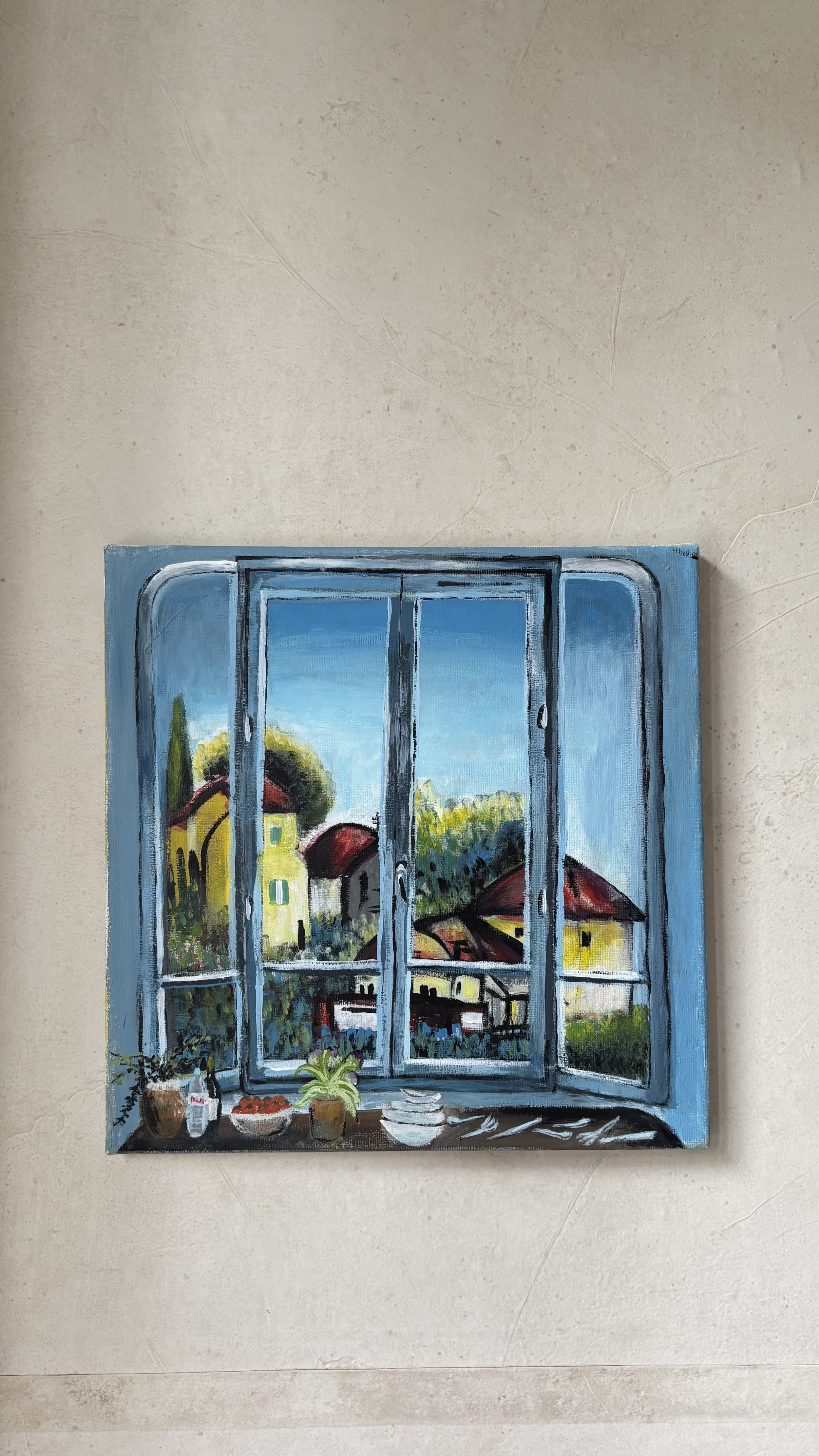 Painting of a window overlooking a scenic landscape with trees and houses, on a beige wall.
