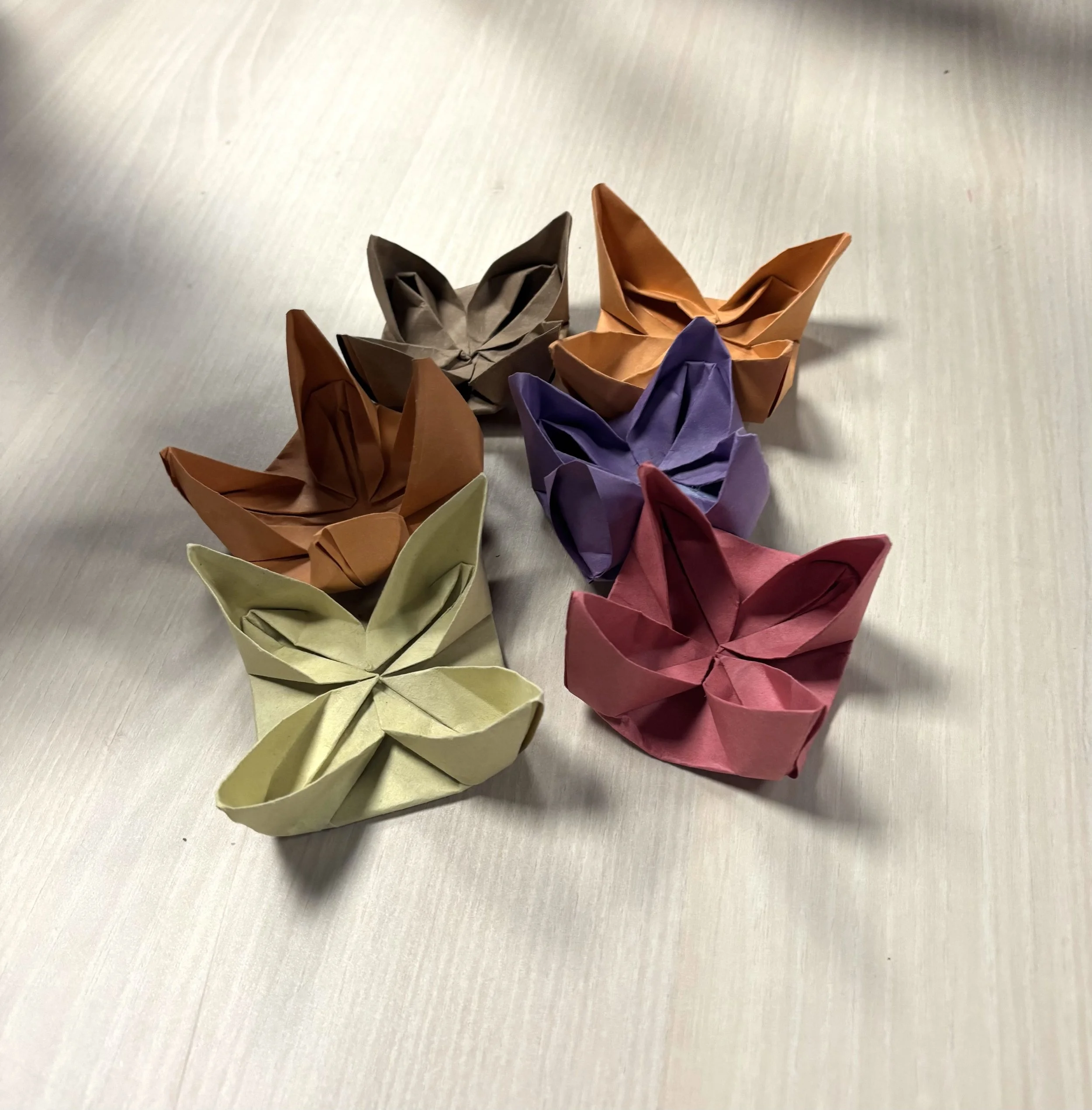Multiple colorful paper origami frogs arranged on a light-colored wooden surface.